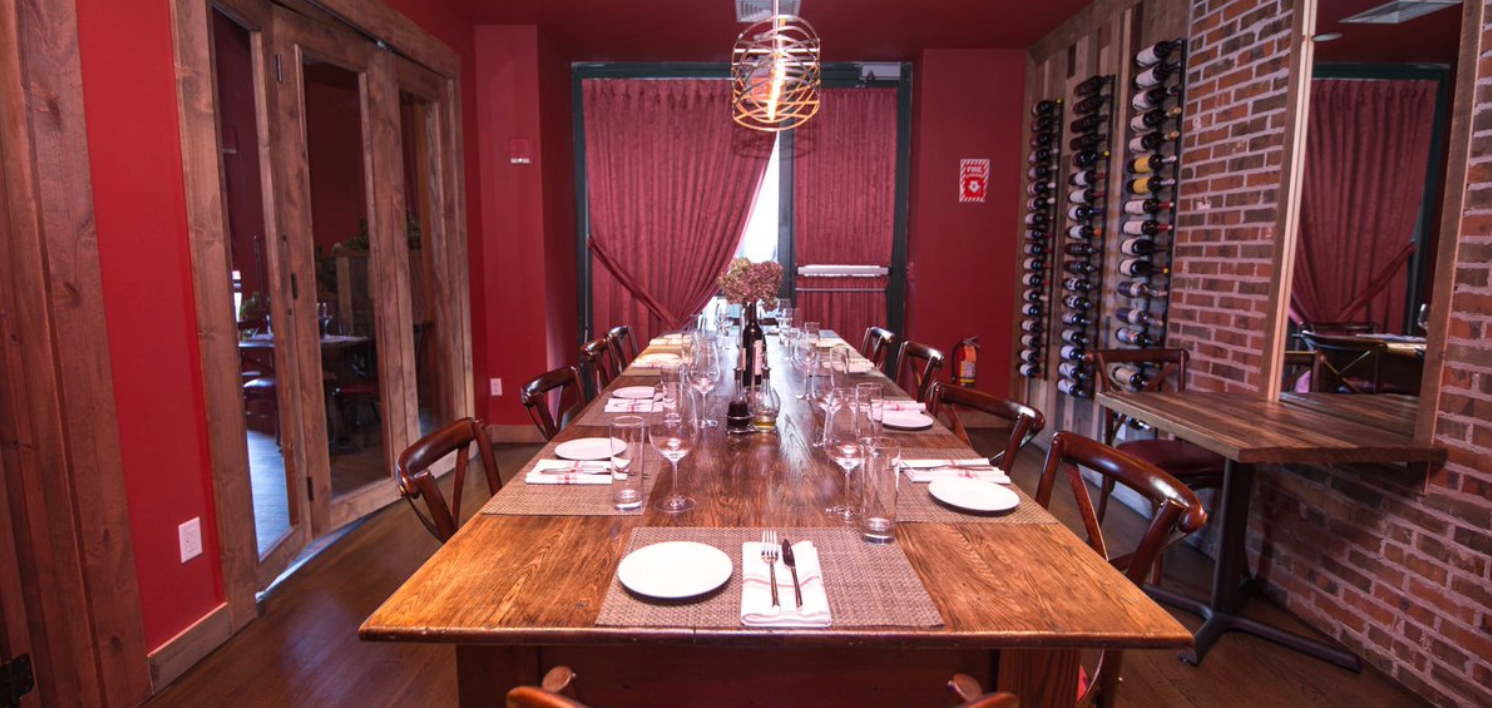 A long wooden dining table set for a meal, in a red-walled room with wood accents.