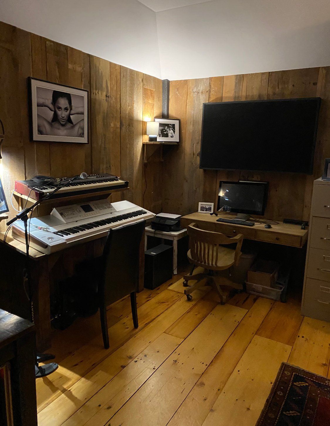 Home office with wood paneling, featuring a desk with keyboard, computer monitor, and TV.