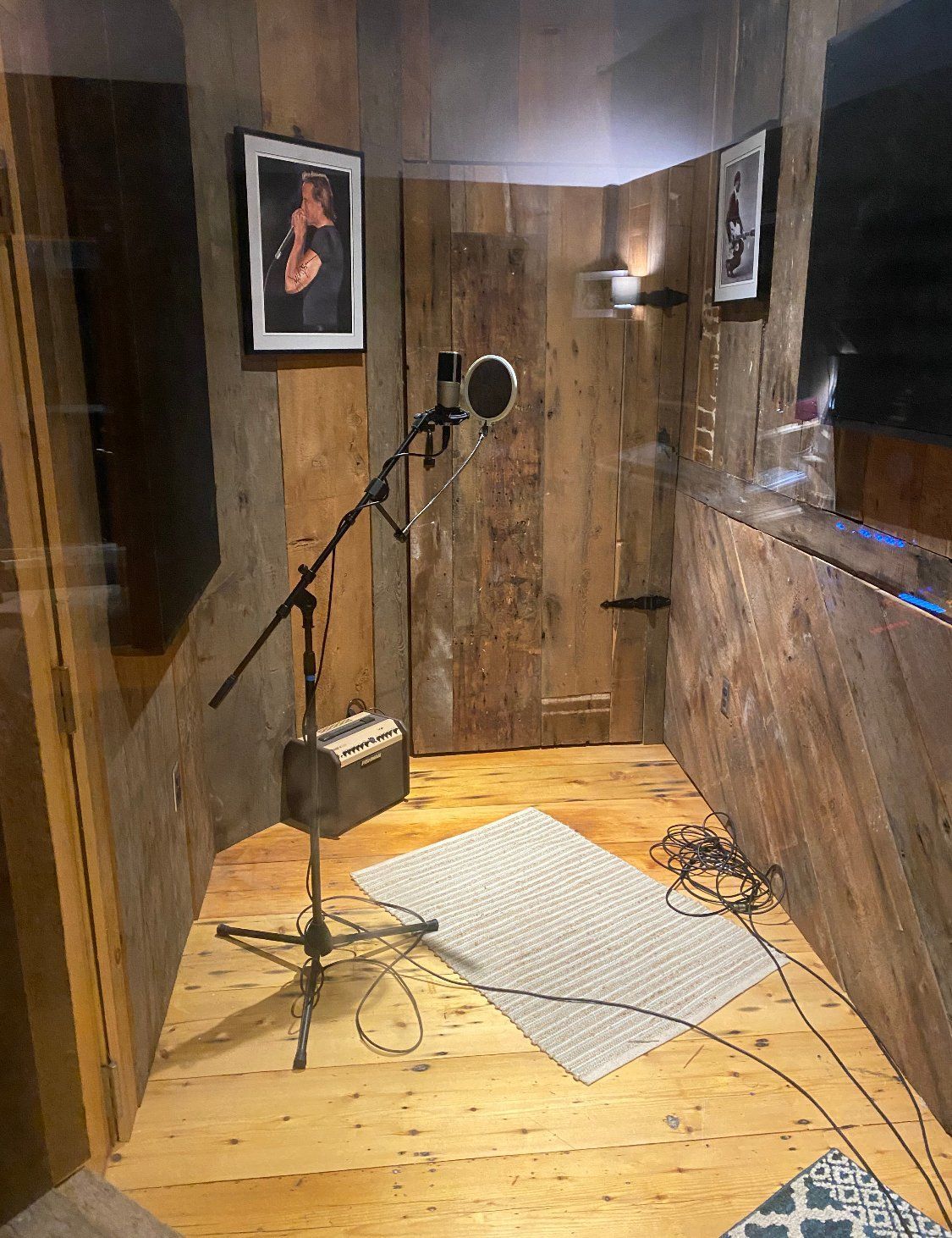 Recording booth with microphone, wooden walls, rug, and artwork.