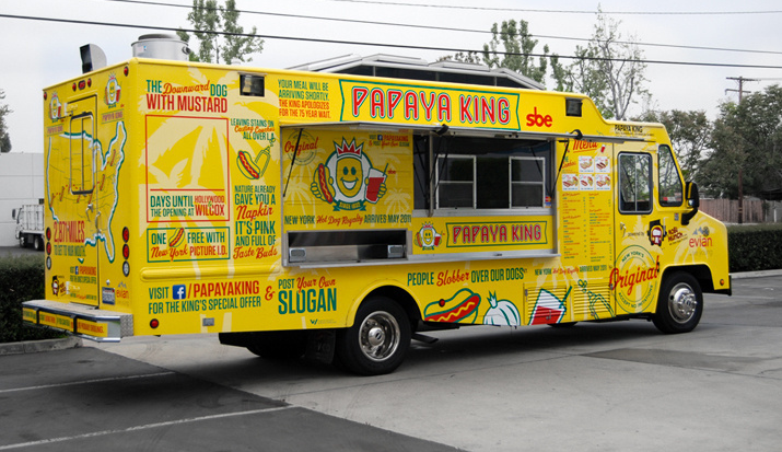 Yellow Papaya King food truck with cartoon artwork, parked outdoors.