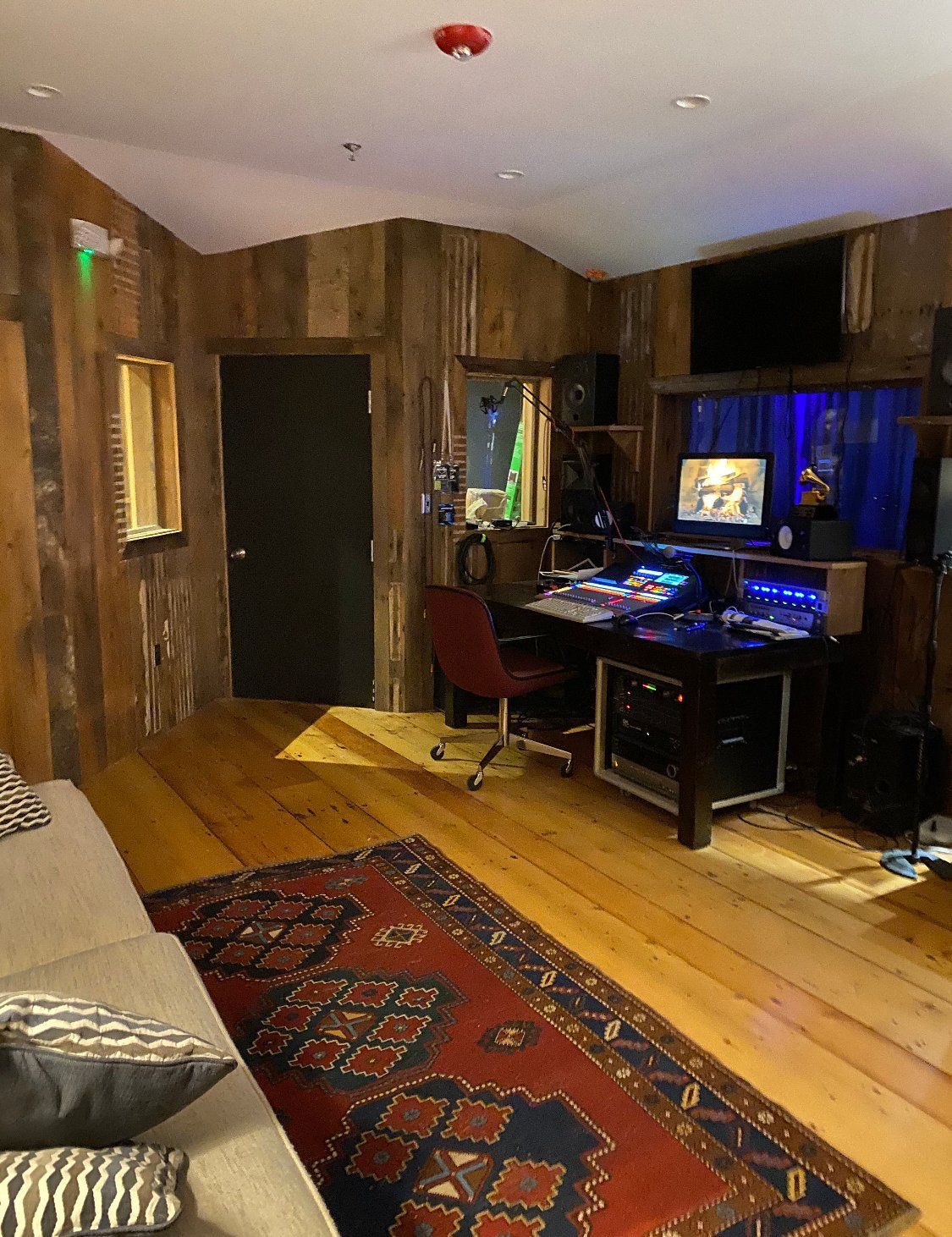 Recording studio with wood paneling, mixing console, and rug.