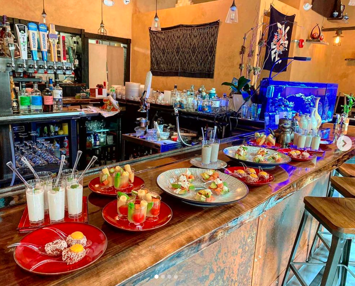 Bar with food, cocktails, and liquor bottles. Wooden bar, red plates, green and blue drinks.