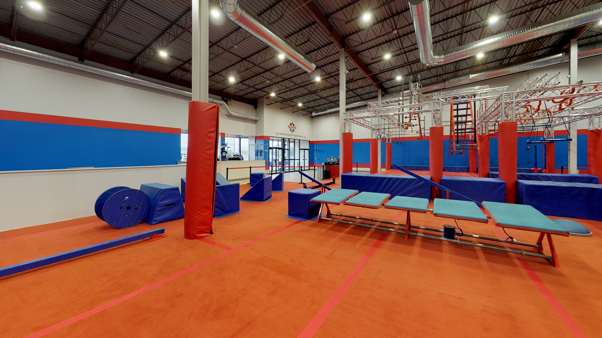Indoor obstacle course with red and blue structures, orange floor, and metal bars.