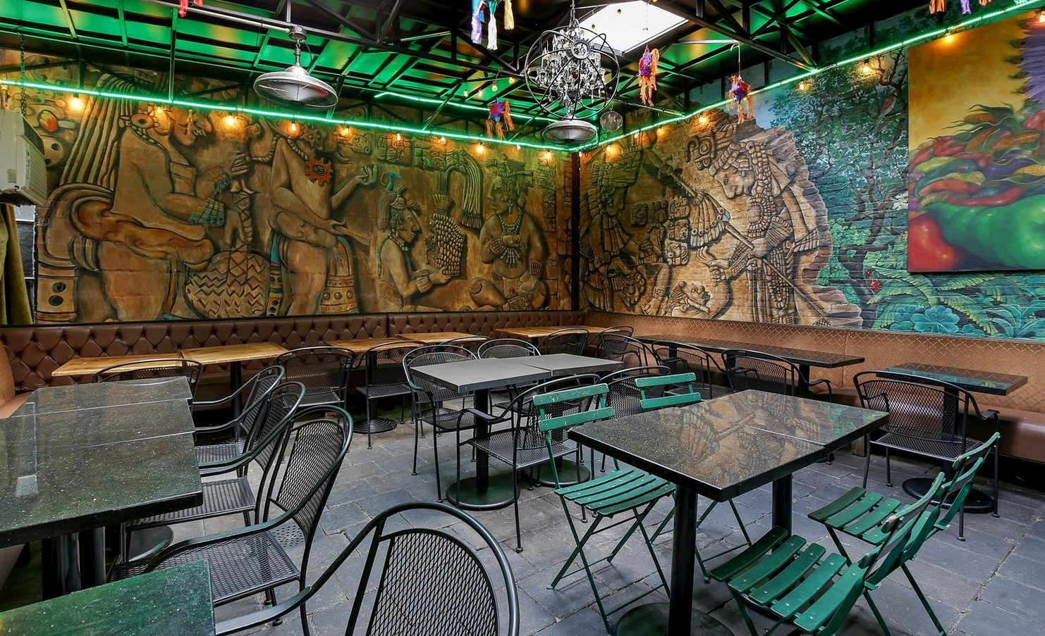 Outdoor dining area with tables and chairs, large mural on wall, green accent lights.