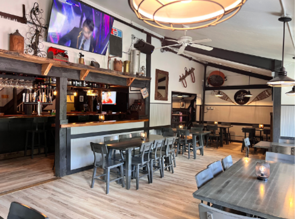 Interior of a restaurant with tables, bar, TV, and decorations; rustic, wood and metal accents.