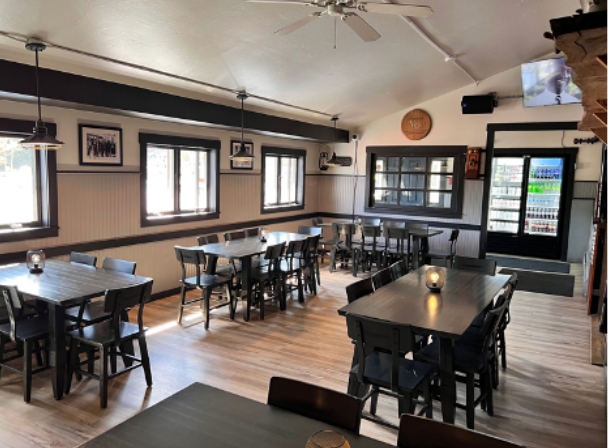 Interior of a restaurant with tables, chairs, windows, and a door. Wooden floors and a neutral color palette.