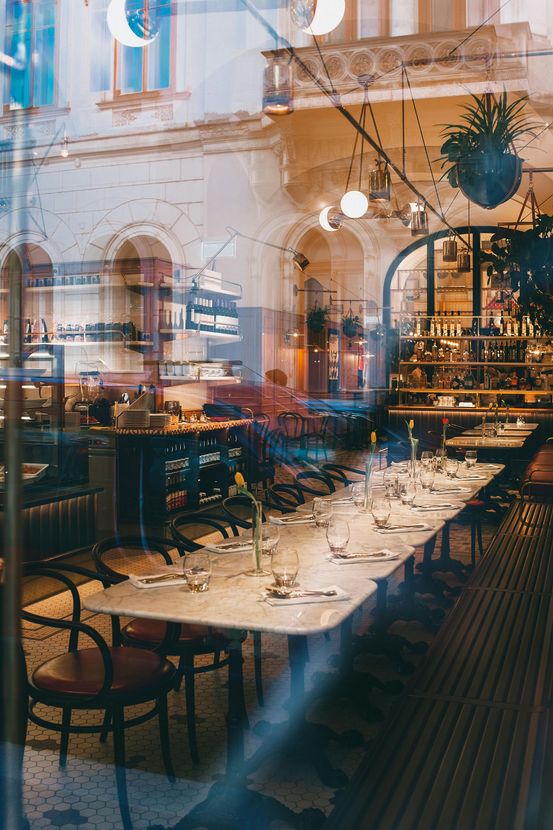 Restaurant interior, tables set for dining, seen through a reflective window. Soft lighting, hints of architecture, chairs visible.