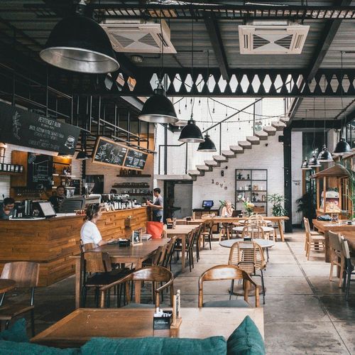 Interior of a coffee shop with wooden tables and chairs, stairs leading up, and bar area.