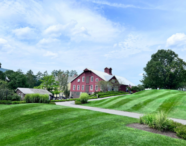 Red barn on a green hill, with striped green lawn and blue sky.