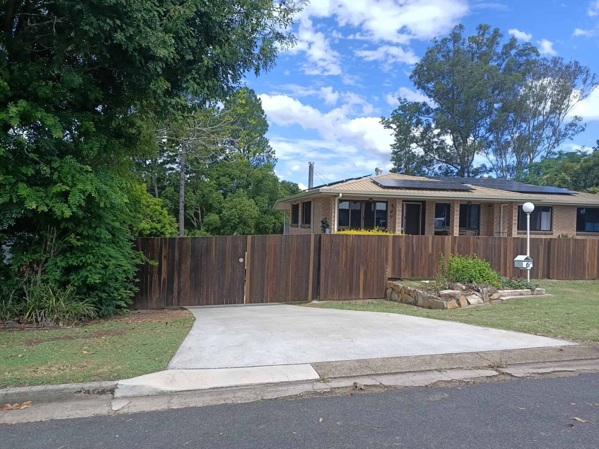 Brown wooden fence encloses a house with solar panels on the roof and a concrete driveway. — Quality Fences 4 U in Gympie, QLD