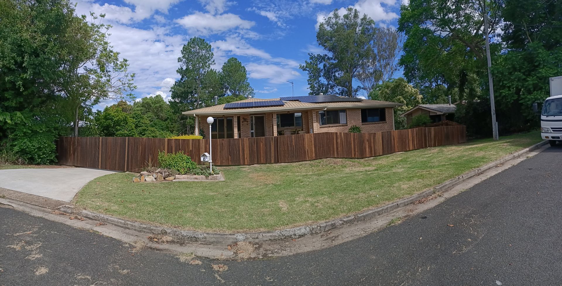 A house with a brown wooden fence, green lawn, and blue sky. A delivery truck is parked on the side — Quality Fences 4 U in Gympie, QLD