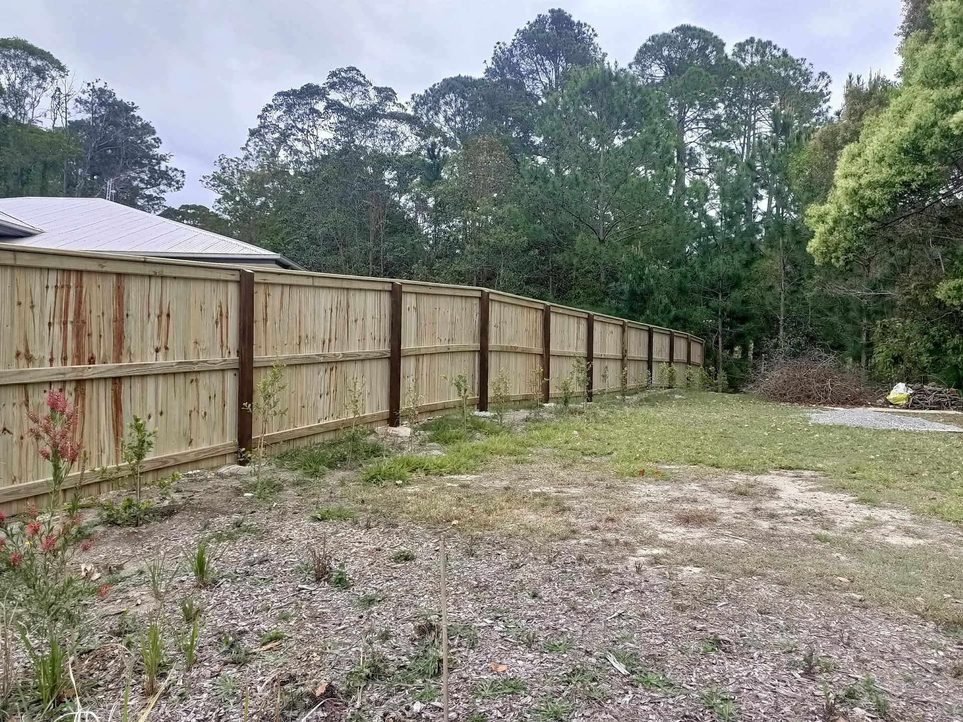 A wooden fence borders a grassy area with trees in the background. Cloudy sky — Quality Fences 4 U in Gympie, QLD