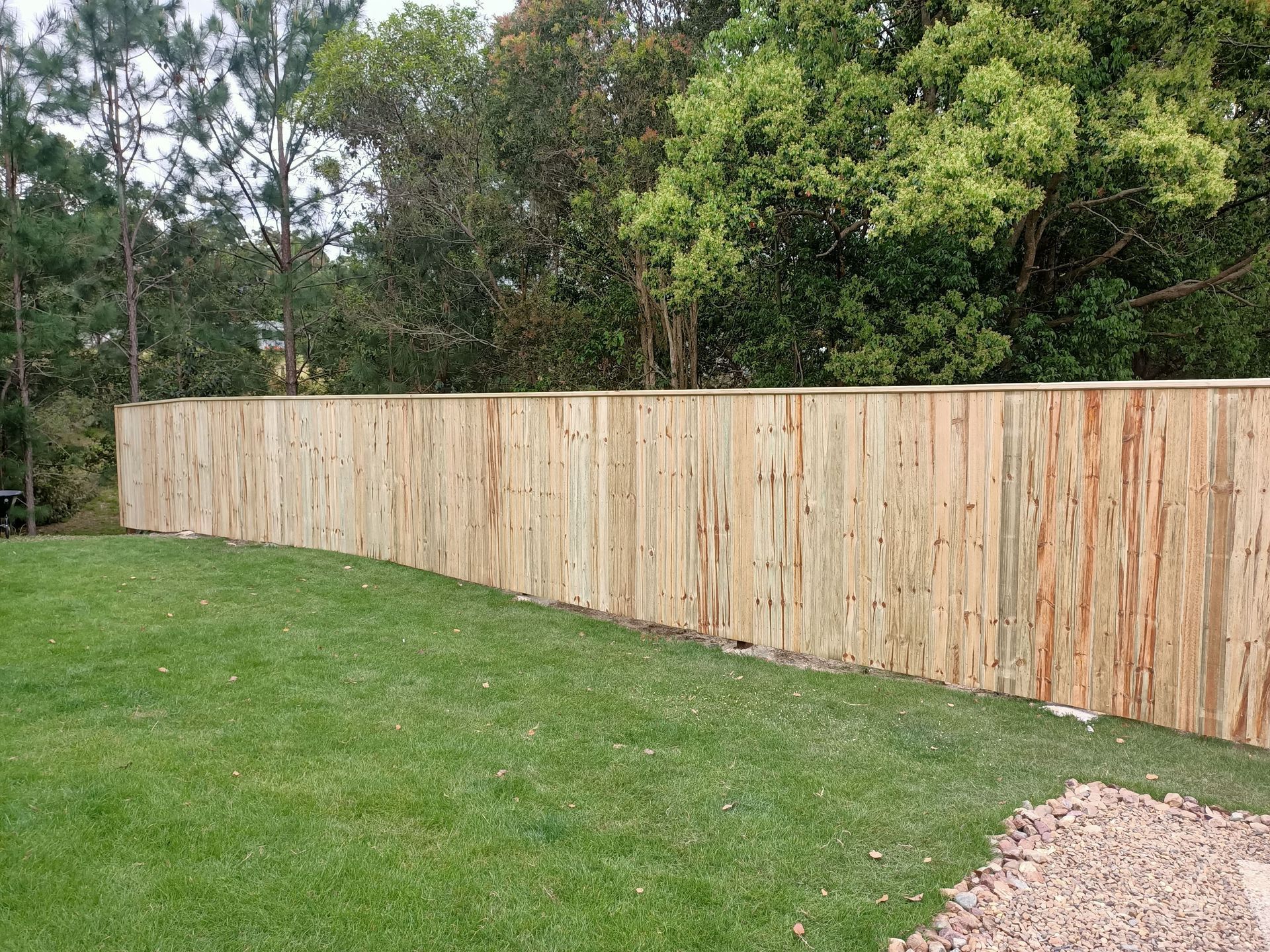 Wooden fence curves around a green grassy yard, with trees in the background — Quality Fences 4 U in Gympie, QLD