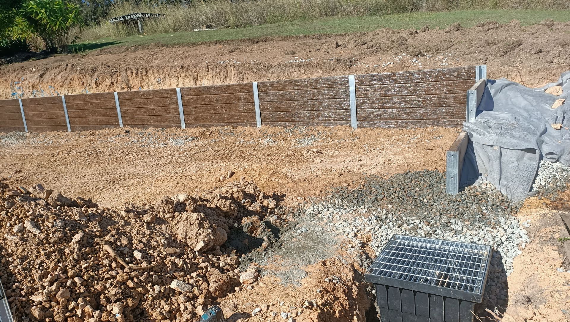 Construction site: retaining wall made of wooden planks held by metal posts, next to a gravel drainage area — Quality Fences 4 U in Gympie, QLD