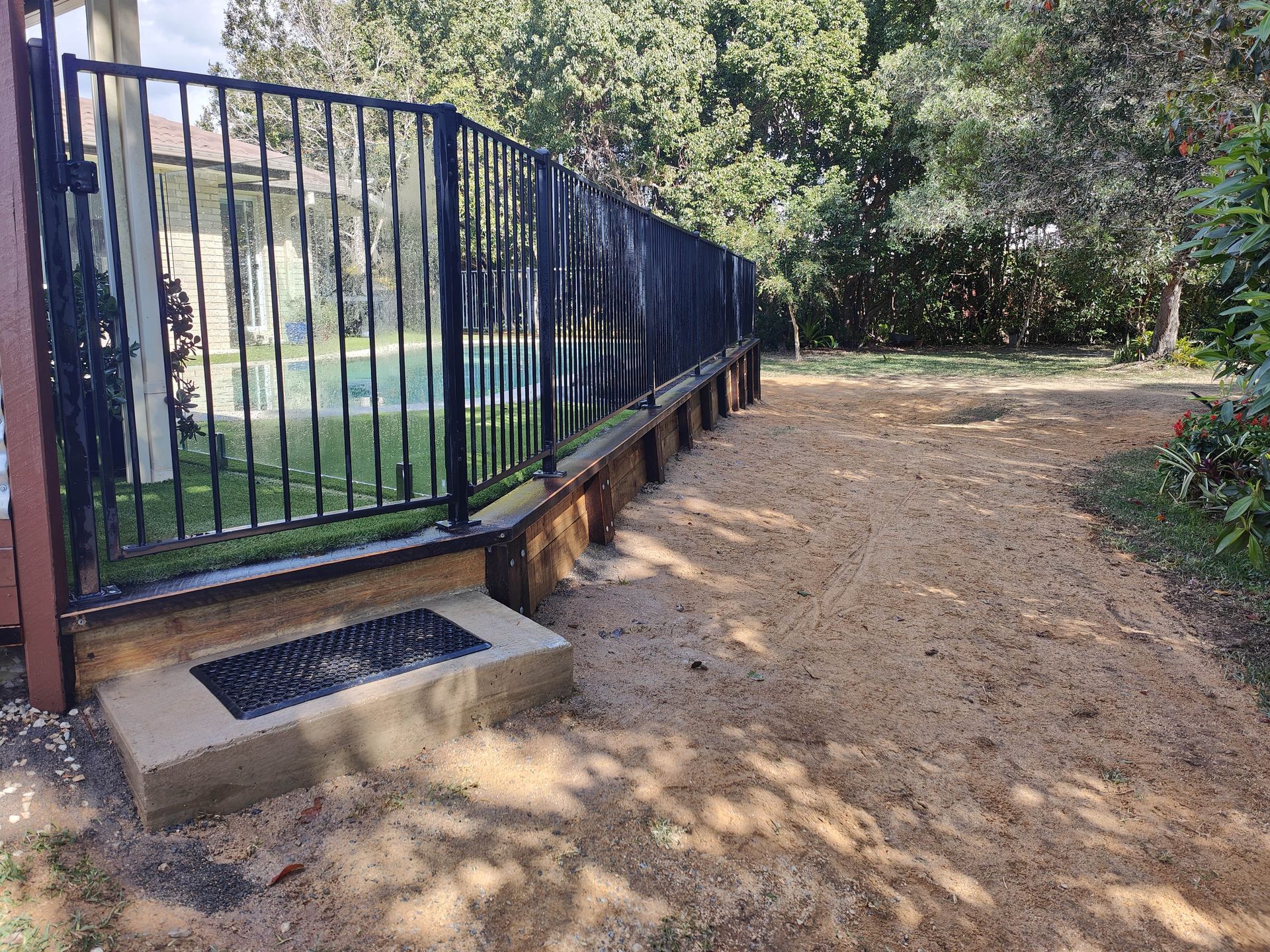 Black metal fence along a dirt area; adjacent to a concrete step. Trees in background — Quality Fences 4 U in Gympie, QLD