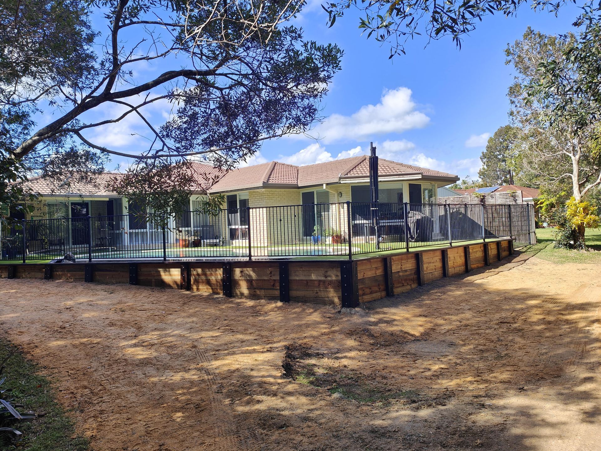 House with a brown roof and wooden retaining wall, black fencing, and dirt ground — Quality Fences 4 U in Gympie, QLD