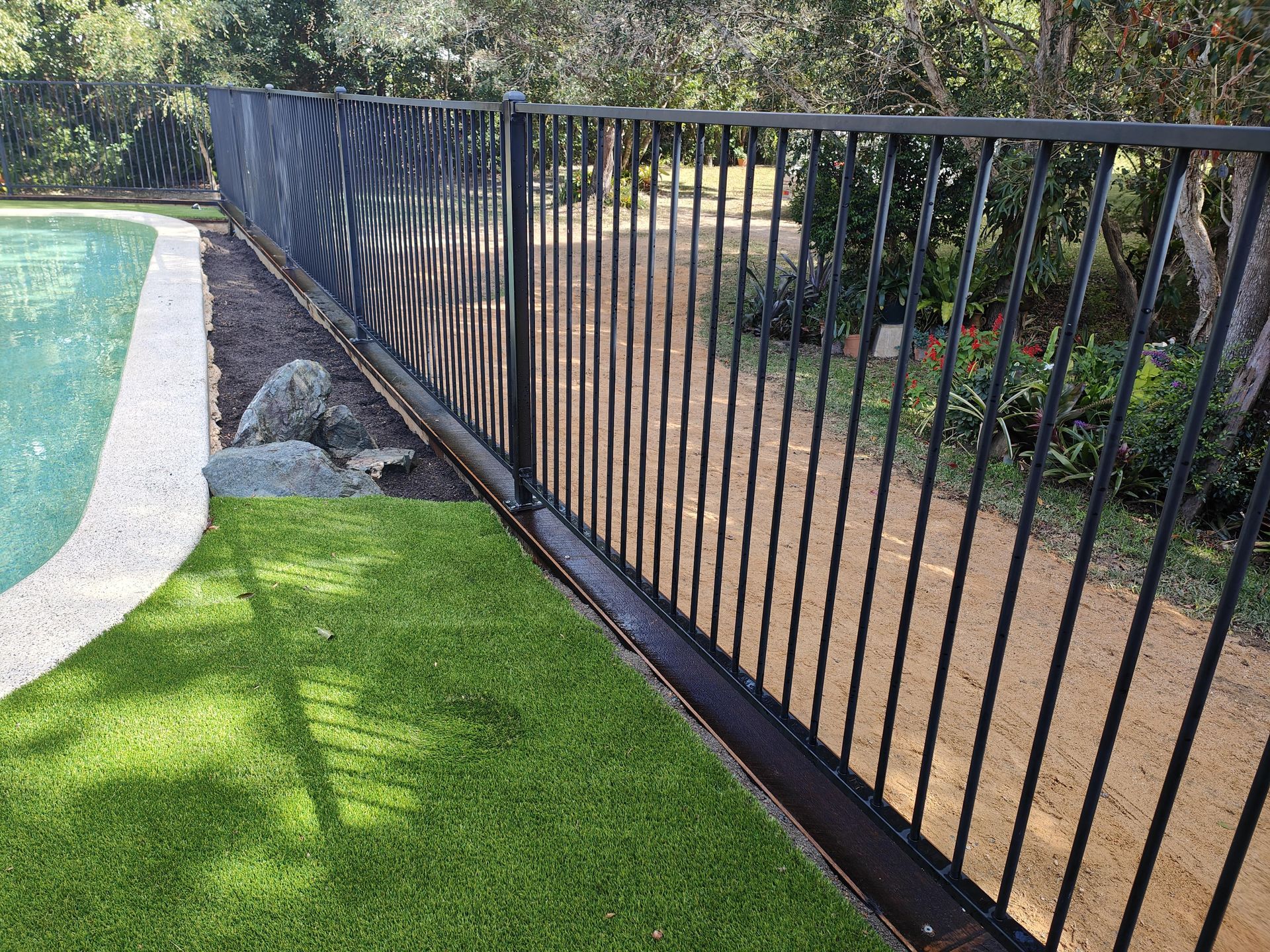 Black metal fence next to a pool and artificial grass, with a path in the background — Quality Fences 4 U in Gympie, QLD