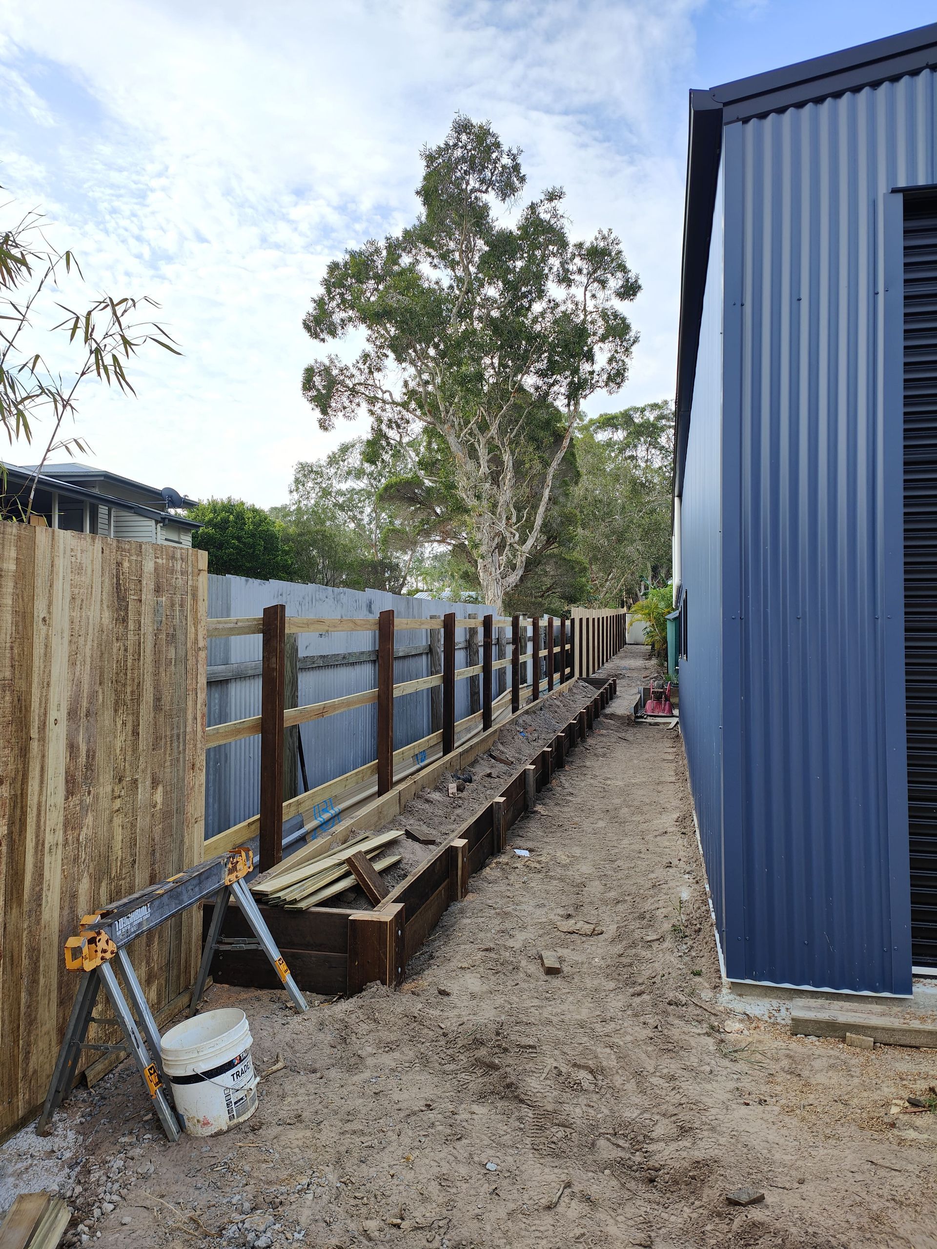 A narrow backyard with a wooden planter box along a fence and a blue corrugated metal building — Quality Fences 4 U in Gympie, QLD