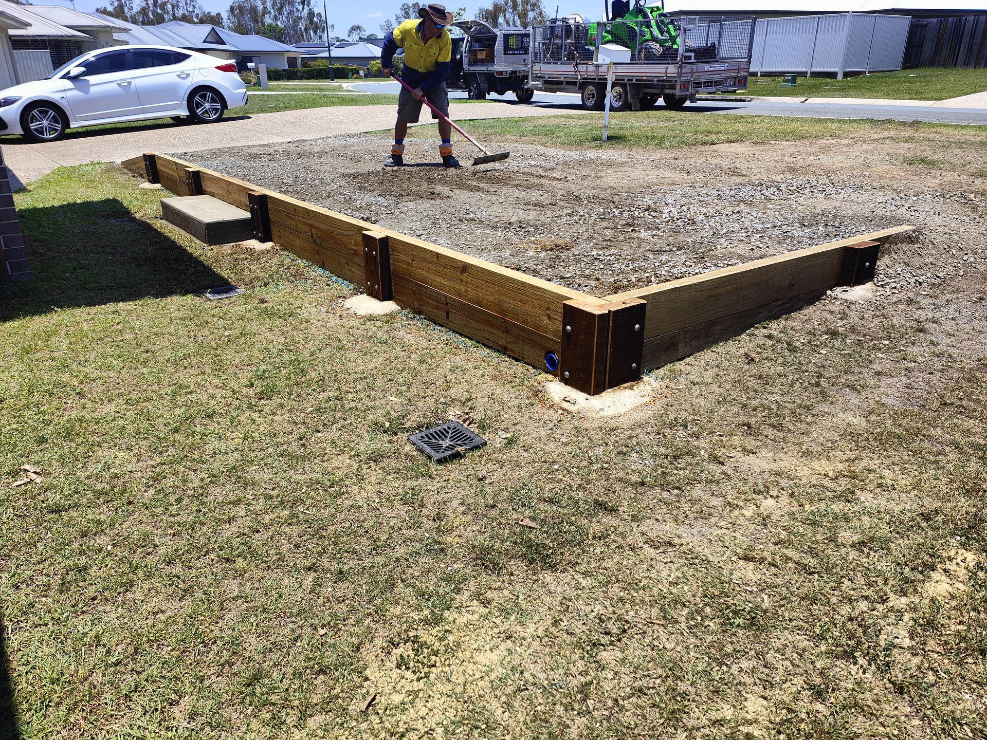 Raised wooden garden bed being prepped with gravel, with a person raking — Quality Fences 4 U in Gympie, QLD
