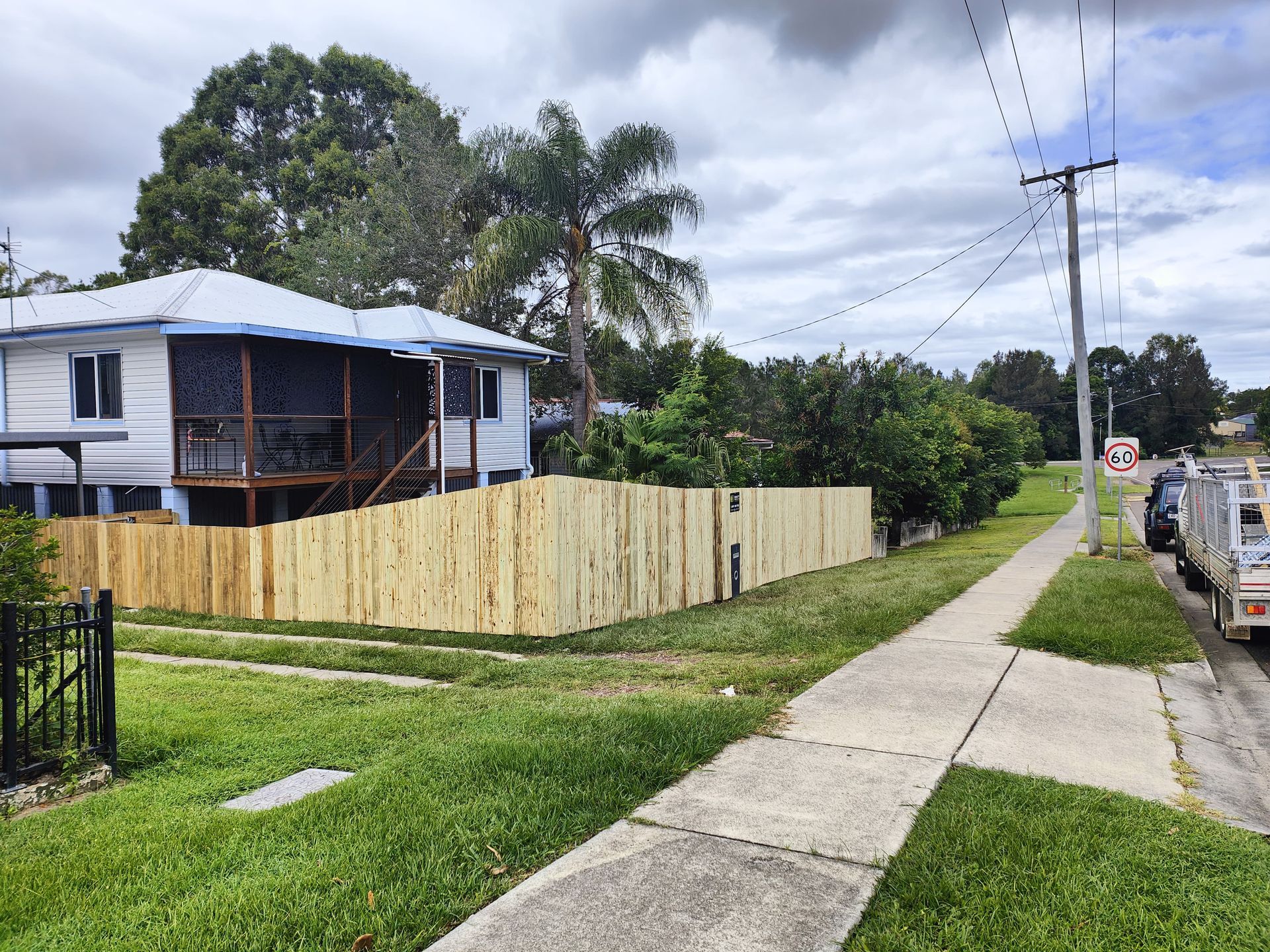 A wooden fence surrounds a white house with a screened-in porch, next to a sidewalk and road — Quality Fences 4 U in Gympie, QLD