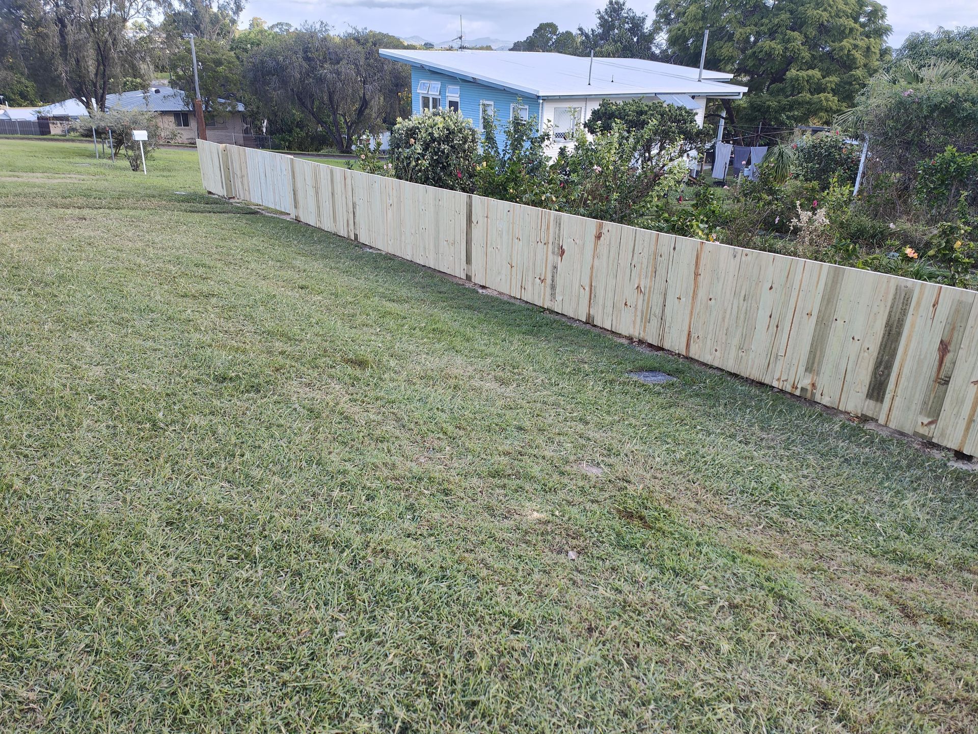 Wooden fence in a grassy yard, with a blue house and trees in the background — Quality Fences 4 U in Gympie, QLD