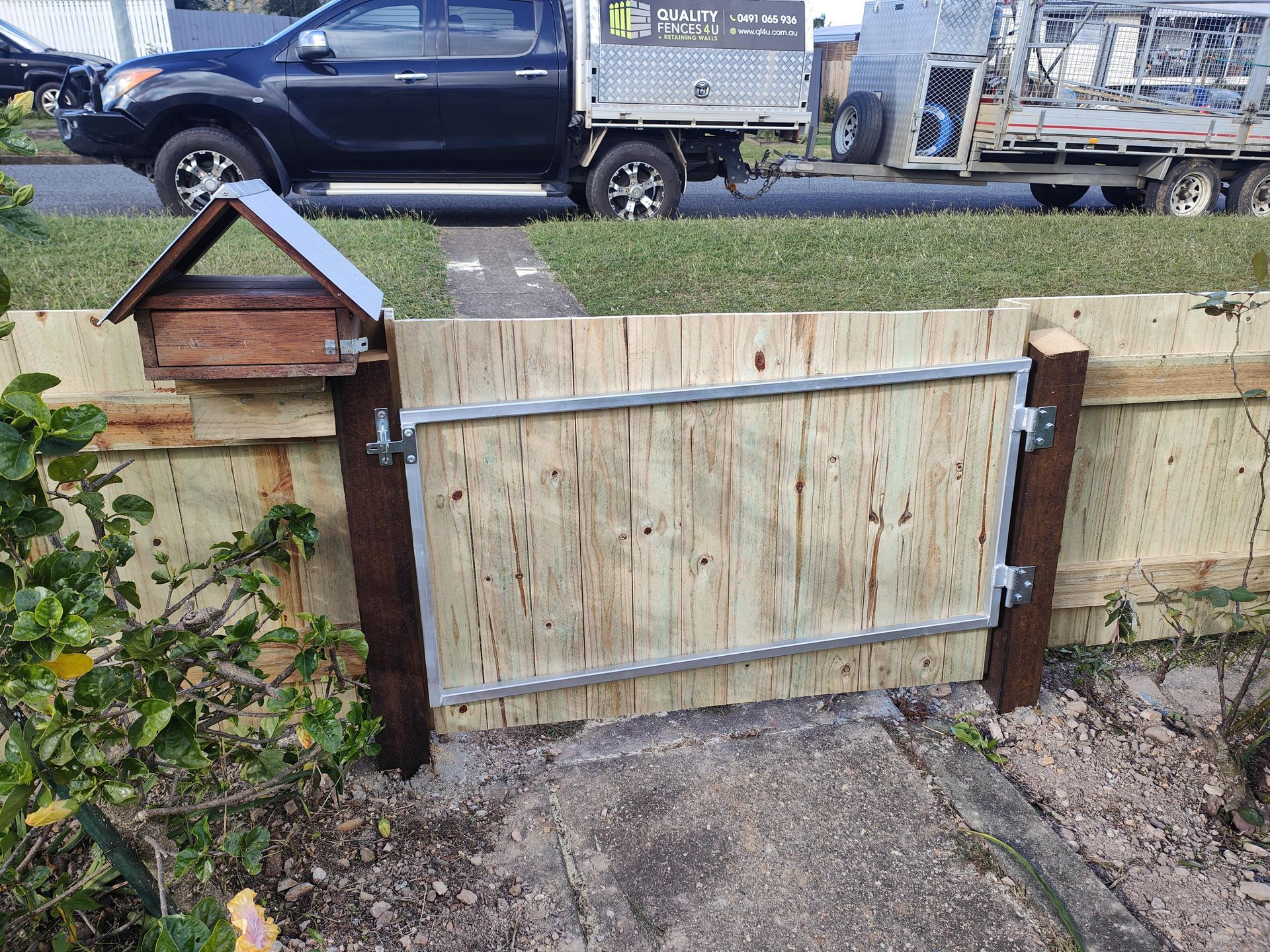 Wooden gate in a fence, with a mailbox attached. A truck and trailer are visible in the background — Quality Fences 4 U in Gympie, QLD