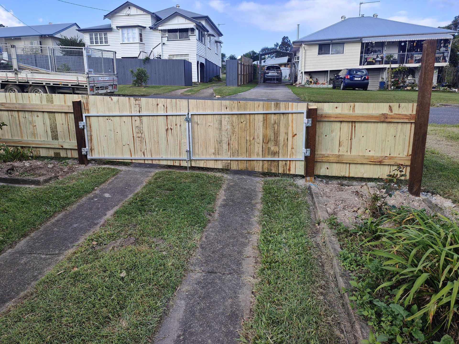 Wooden driveway gate; weathered, light brown boards, metal hardware, grass and concrete path in front — Quality Fences 4 U in Gympie, QLD