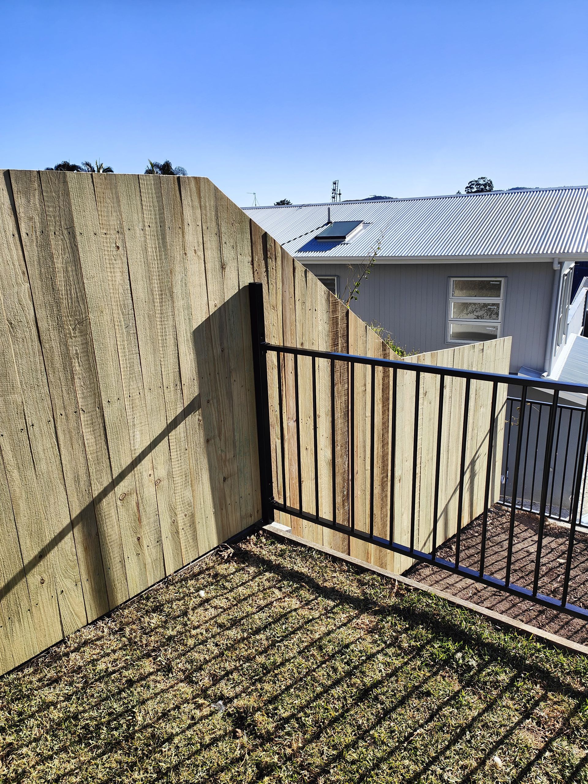 View from a patio with a textured concrete wall, wooden fence, black metal railing, and a house in the background — Quality Fences 4 U in Gympie, QLD