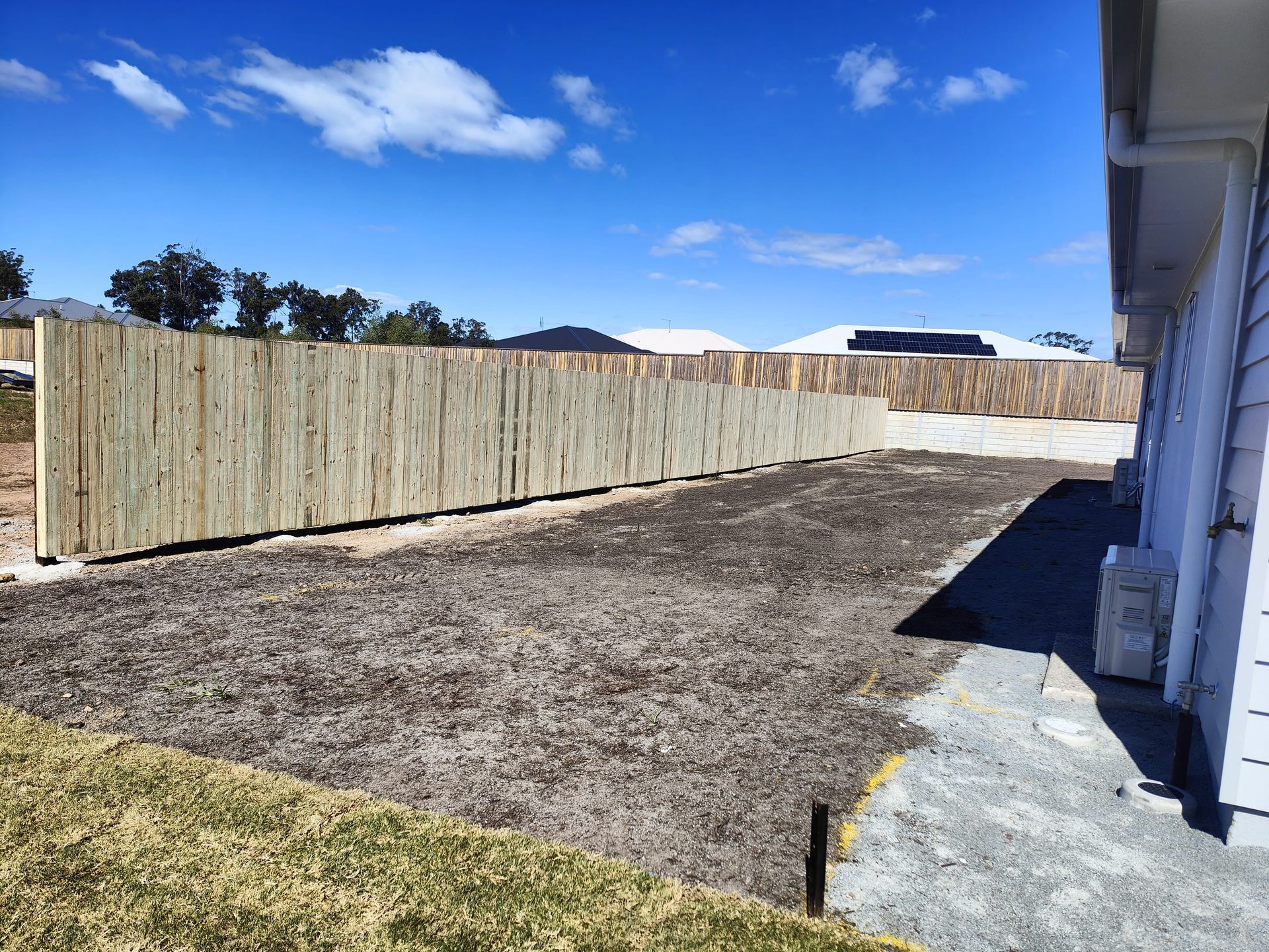 Wooden fence lines a dirt yard beside a house under a blue sky — Quality Fences 4 U in Gympie, QLD
