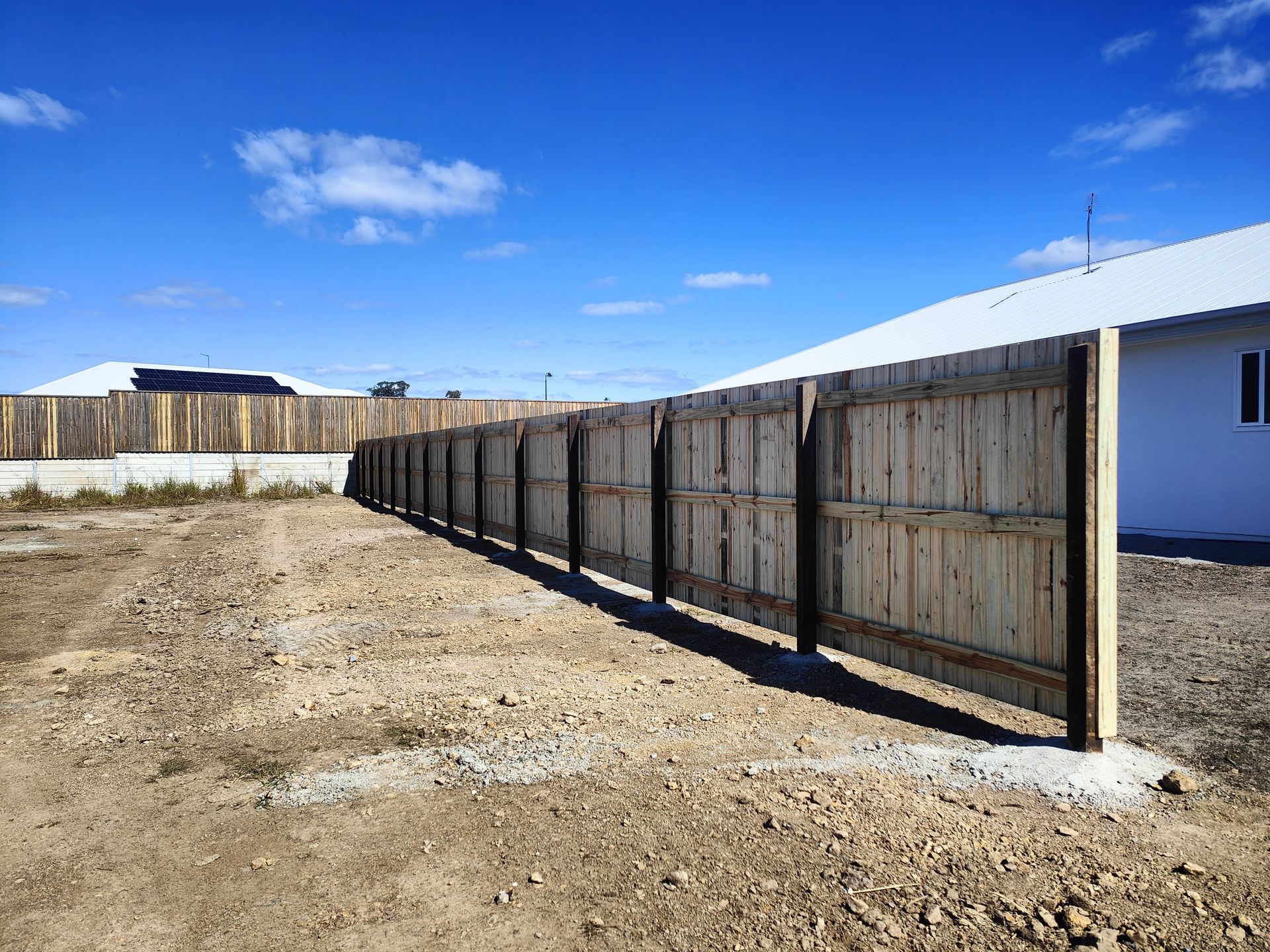 Wooden fence in a bare, dirt yard next to a white house under a blue sky — Quality Fences 4 U in Gympie, QLD