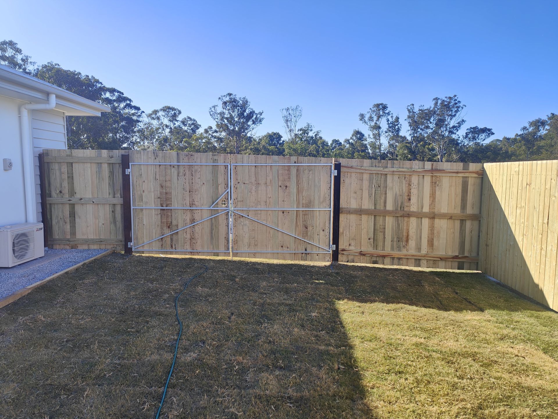 Wooden fence with a metal gate in a grassy backyard, clear sky — Quality Fences 4 U in Gympie, QLD