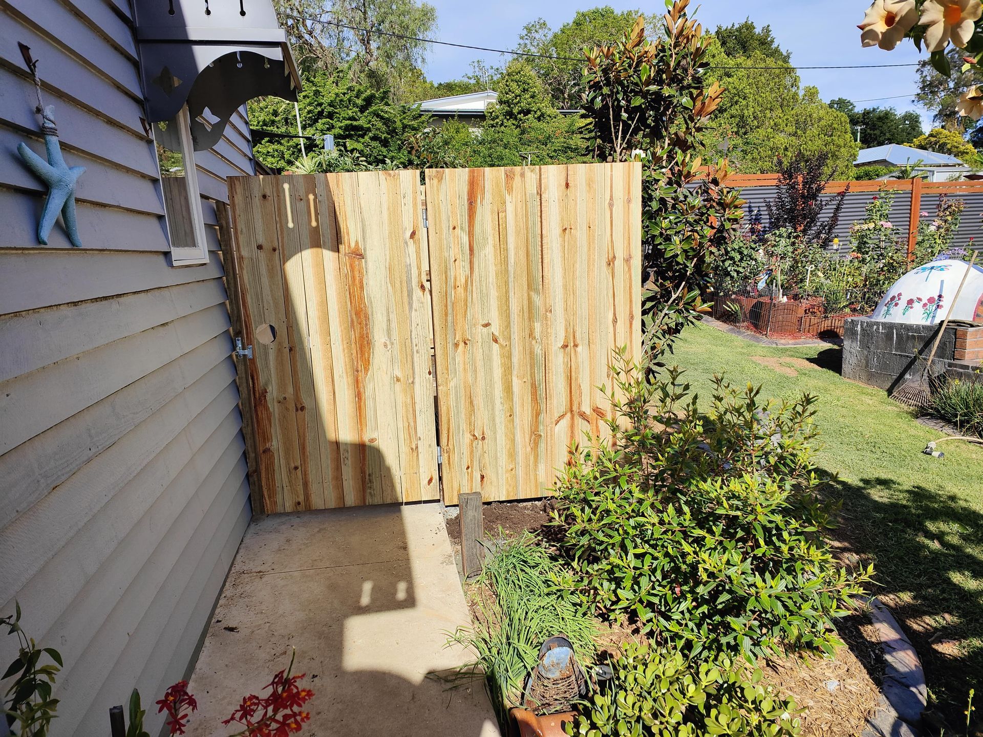Wooden gate next to a house, separating the area from the garden. Green foliage and concrete pathway are visible — Quality Fences 4 U in Gympie, QLD