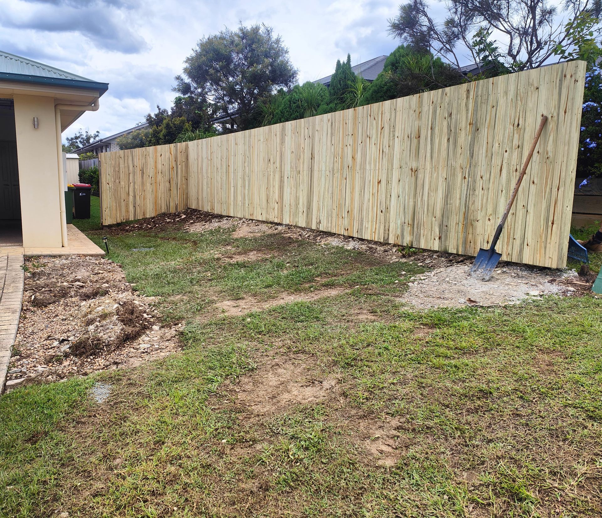 Wooden fence in backyard, built next to a house. Lawn needs attention; shovel rests against the fence — Quality Fences 4 U in Gympie, QLD
