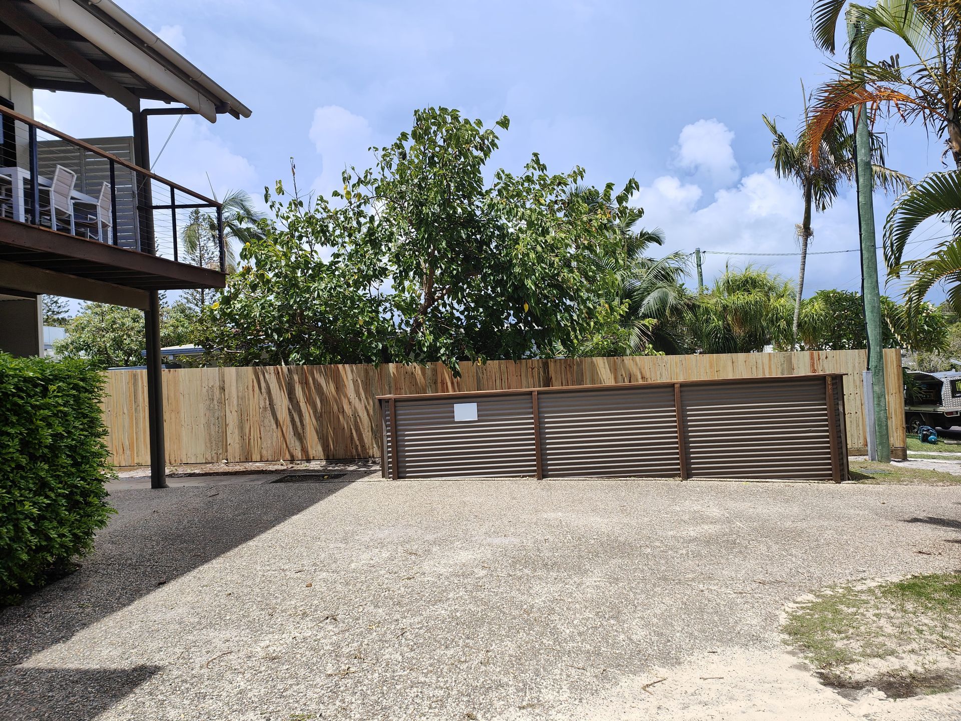 Gravel parking area next to a building with a balcony and wooden fence, under a partly cloudy sky — Quality Fences 4 U in Gympie, QLD