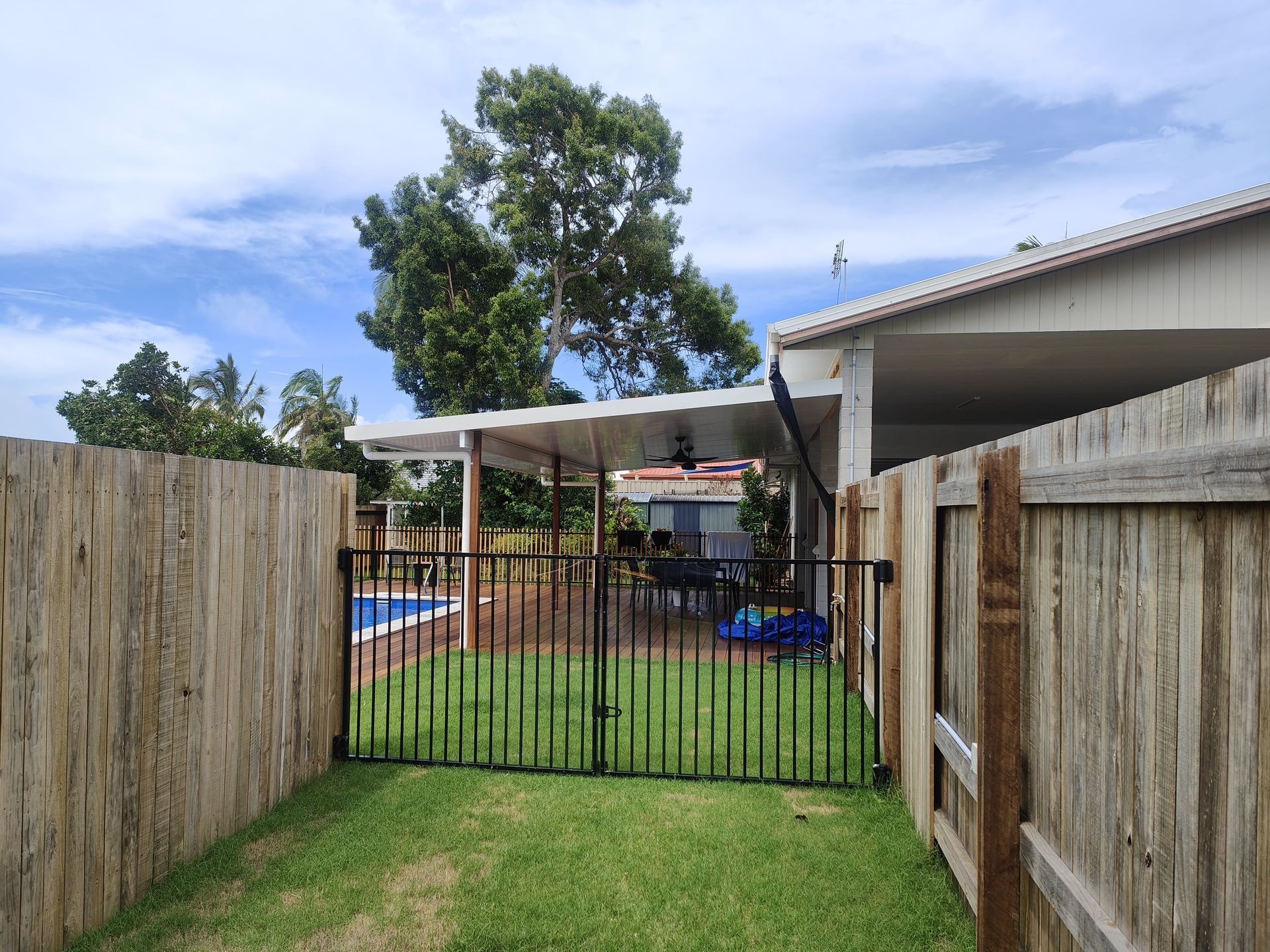 Backyard with fence, gate, patio, pool, and trees under a cloudy sky — Quality Fences 4 U in Gympie, QLD
