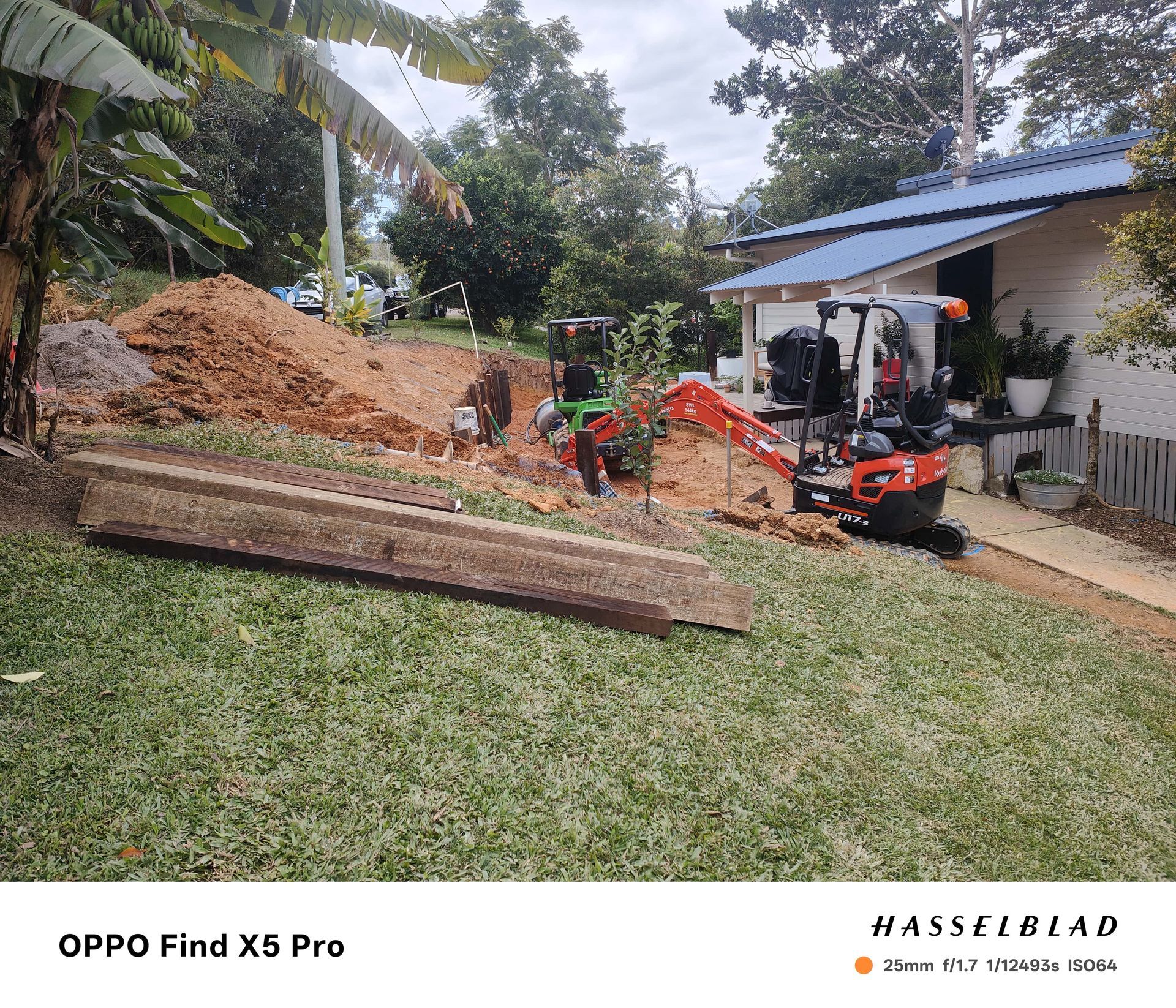 Mini excavator digging earth near a house with a blue roof, and a pile of soil on a lawn — Quality Fences 4 U in Gympie, QLD