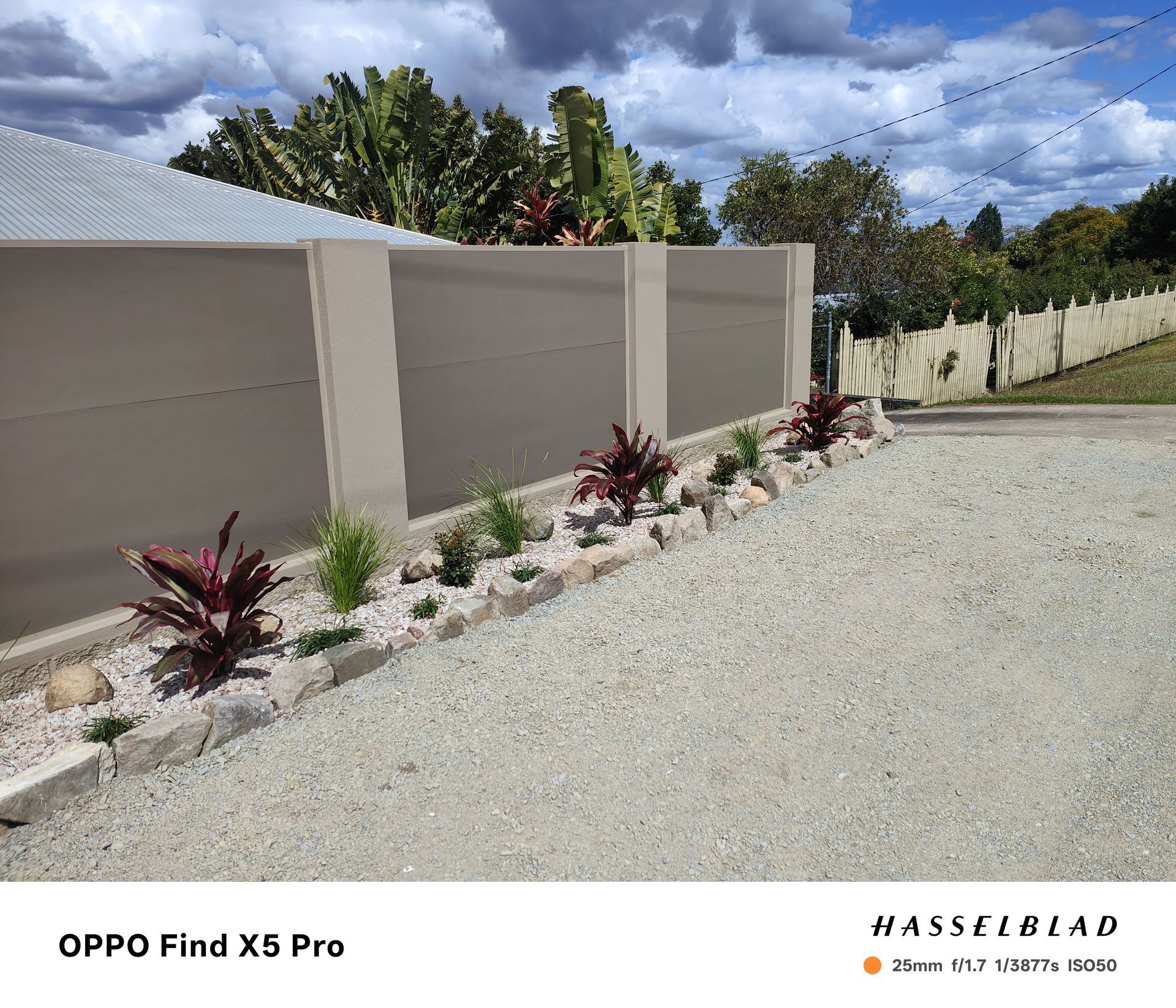 A gravel driveway with a low wall, plants, and a white fence under a cloudy sky — Quality Fences 4 U in Gympie, QLD