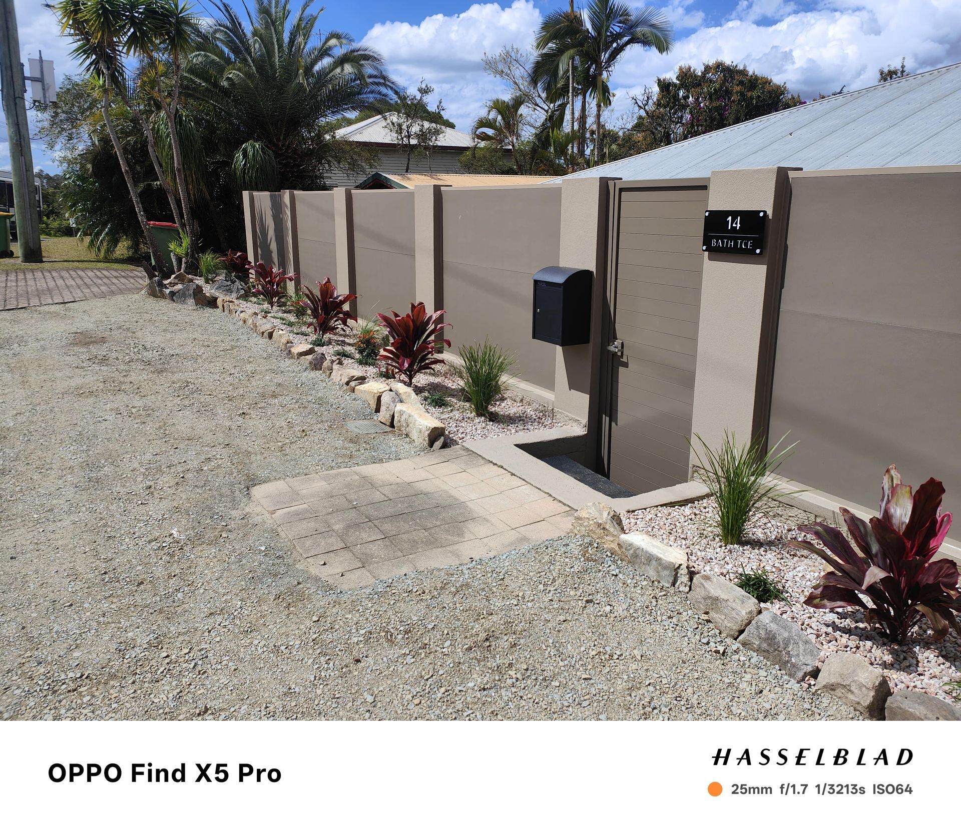 Gravel driveway and beige fence with plants, mailbox, and gated entry on a sunny day — Quality Fences 4 U in Gympie, QLD