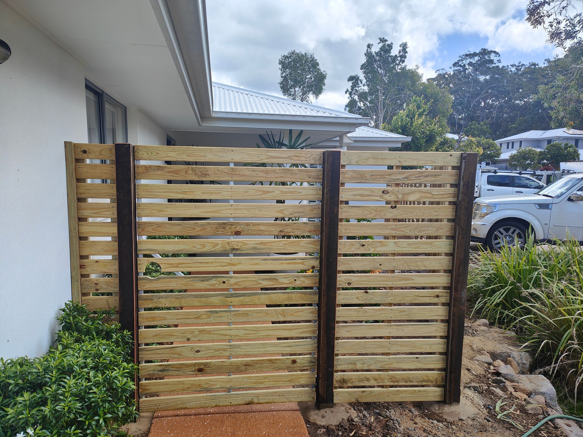 Wooden Slat Gate With Dark Posts Beside A White House And Parked Cars Outdoors — Quality Fences 4 U in Gympie, QLD