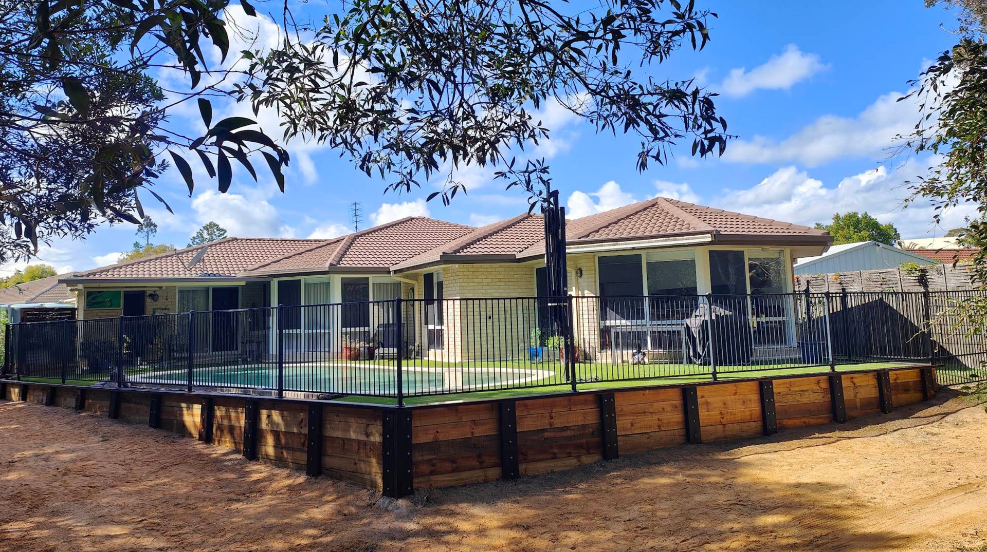 Rectangular swimming pool in a backyard with a bamboo fence and green grass. Cloudy sky.