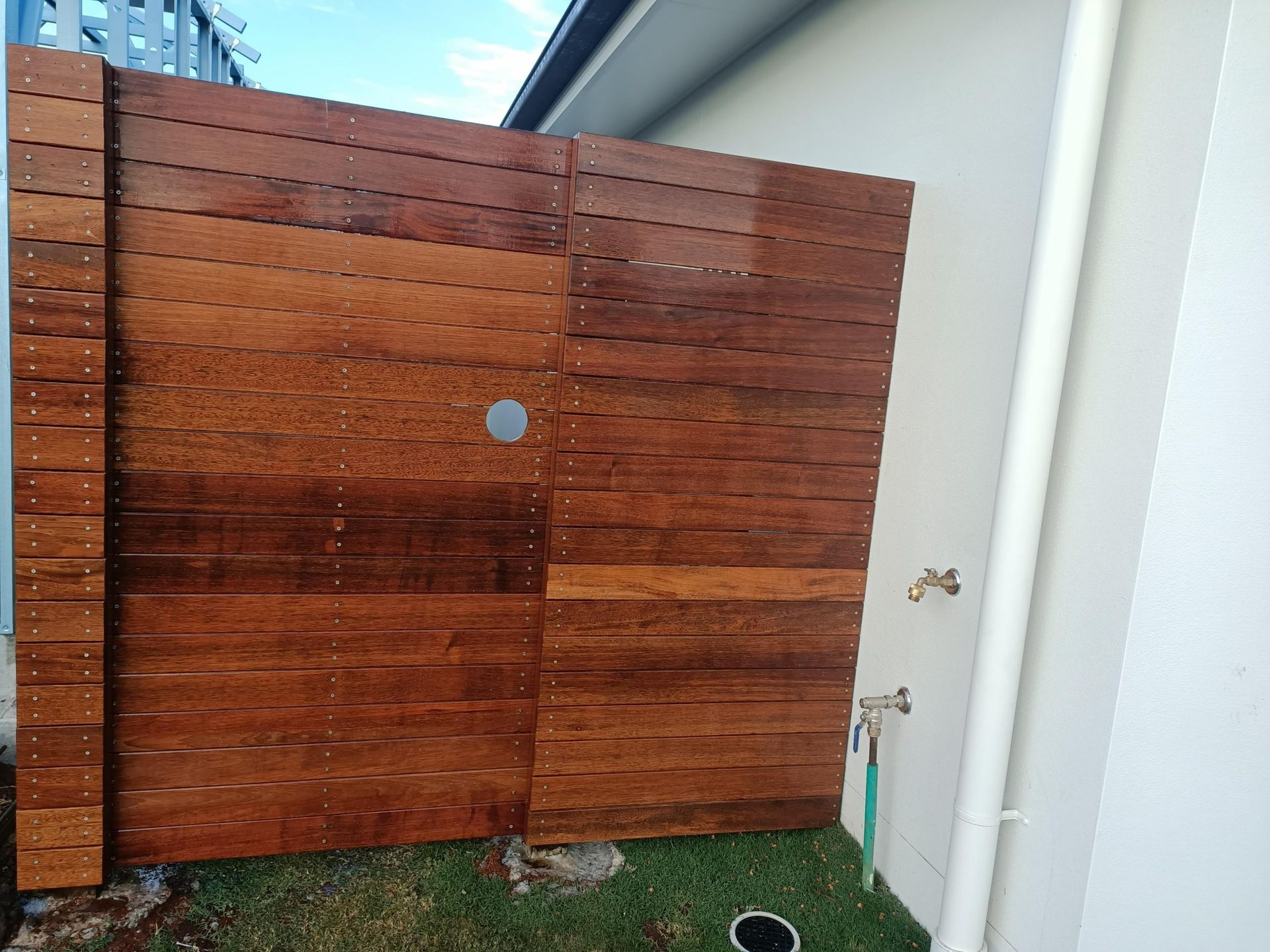 Wooden Fence Against a White Wall With a Pipe and Tap — Quality Fences 4 U in Gympie, QLD