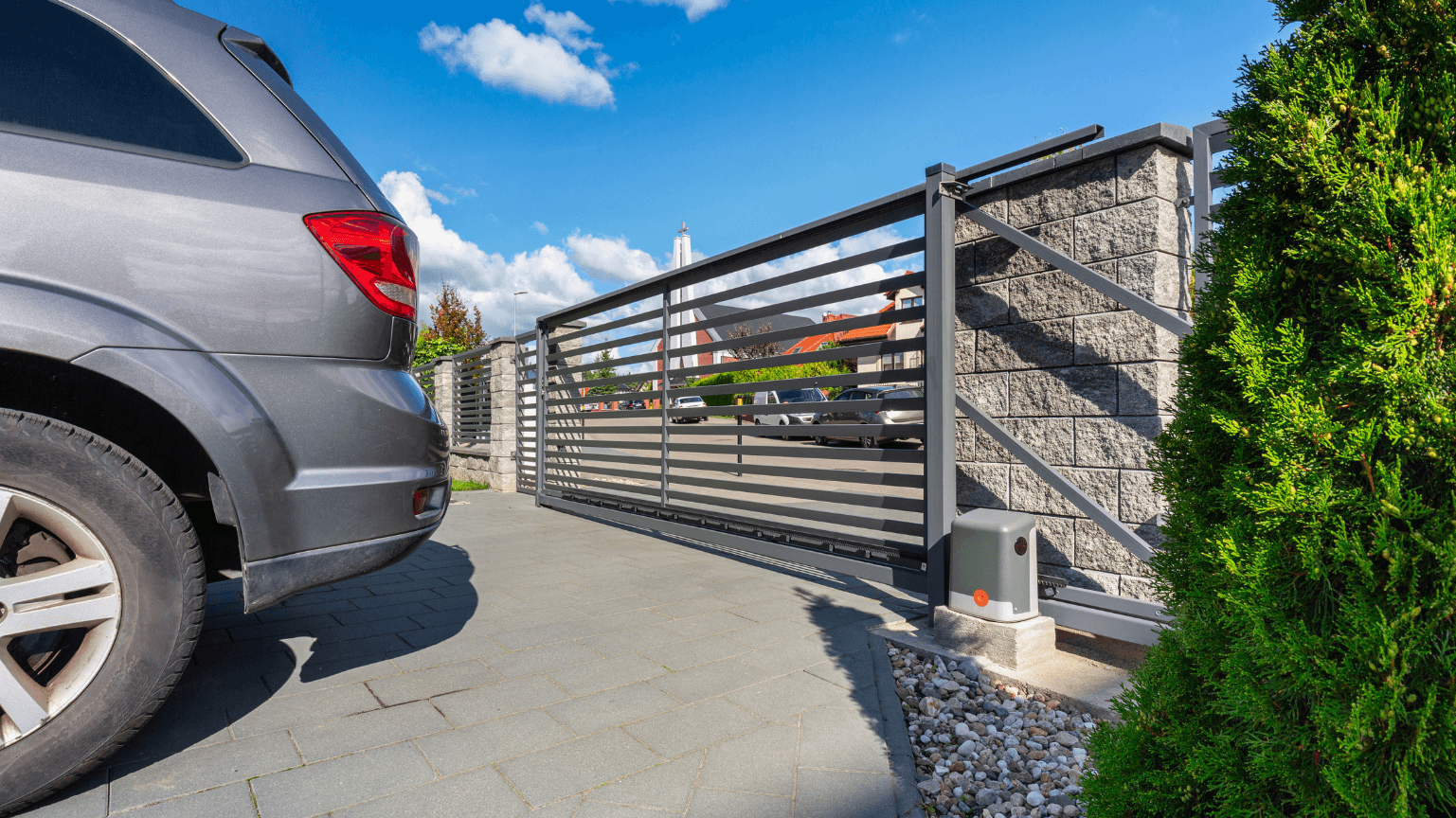 Grey SUV near a sliding metal gate, concrete driveway, stone fence, blue sky — Quality Fences 4 U in Gympie, QLD