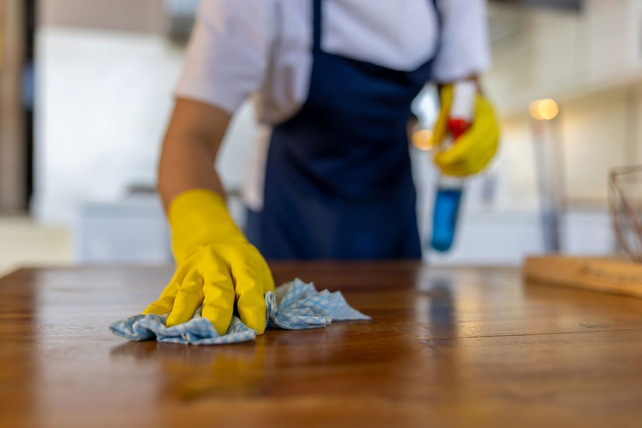 A person wearing yellow gloves is cleaning a wooden table with a cloth.