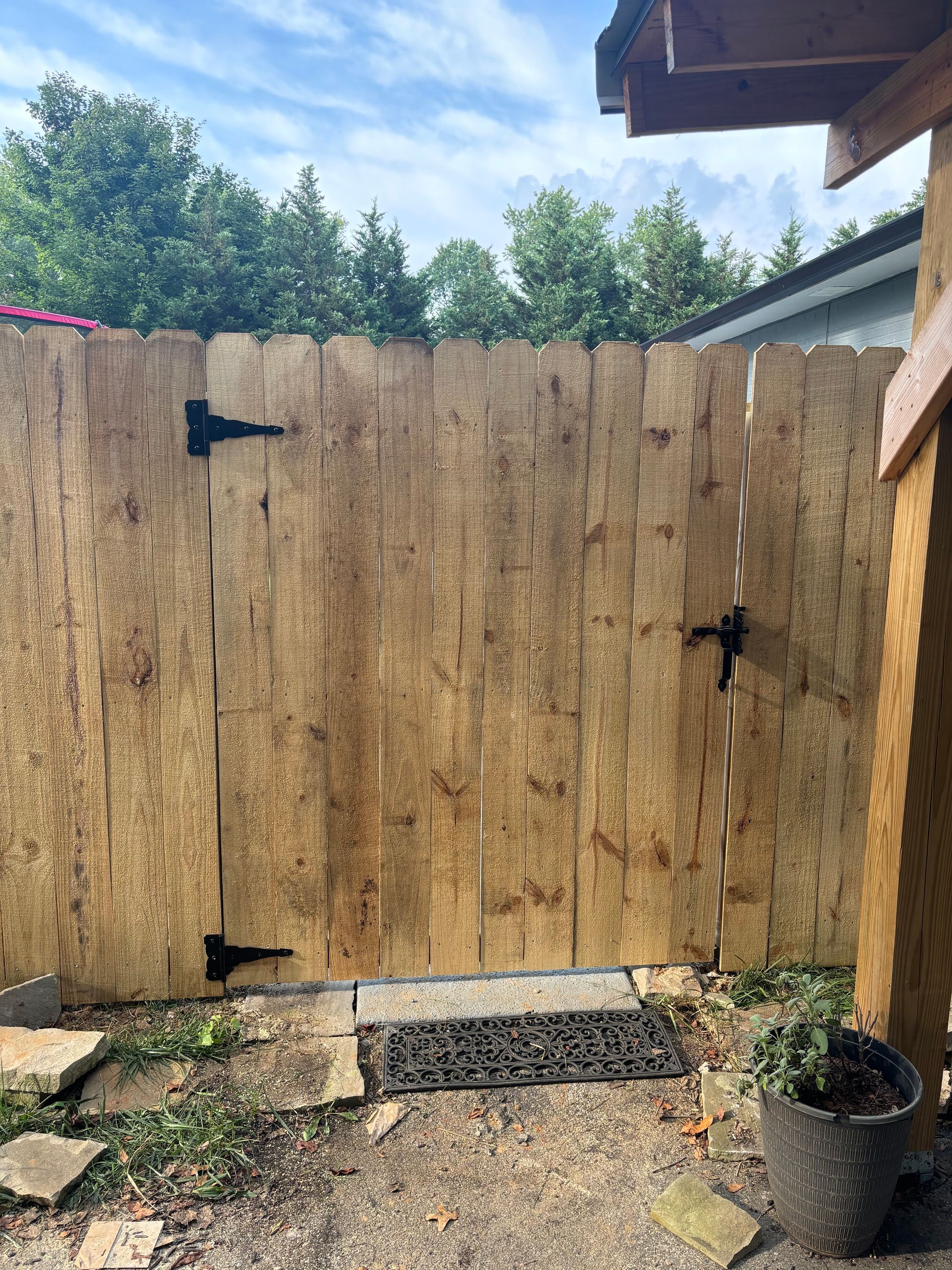 A wooden fence with a black door and a potted plant in front of it.