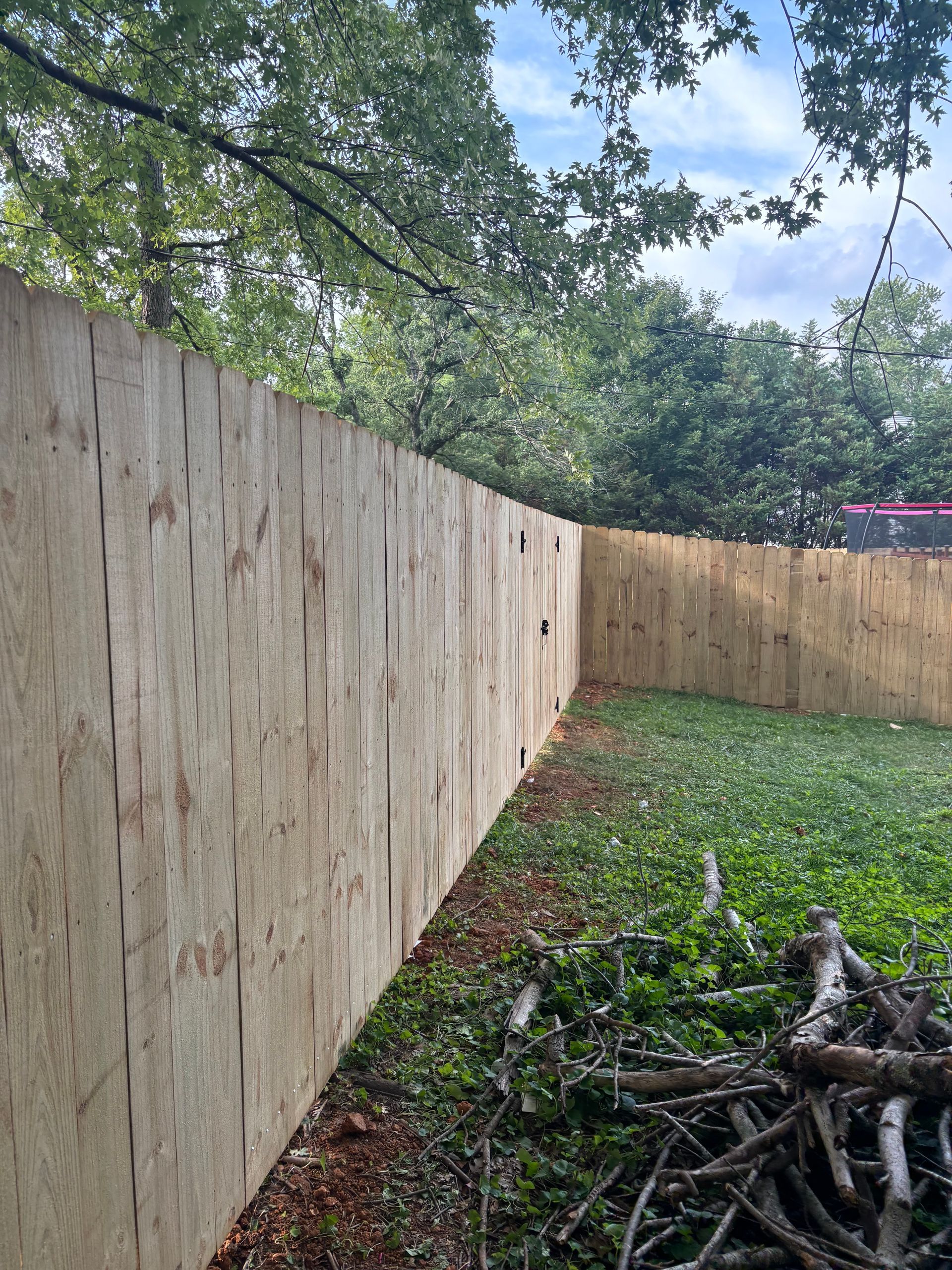 A wooden fence is surrounded by trees and grass in a backyard.