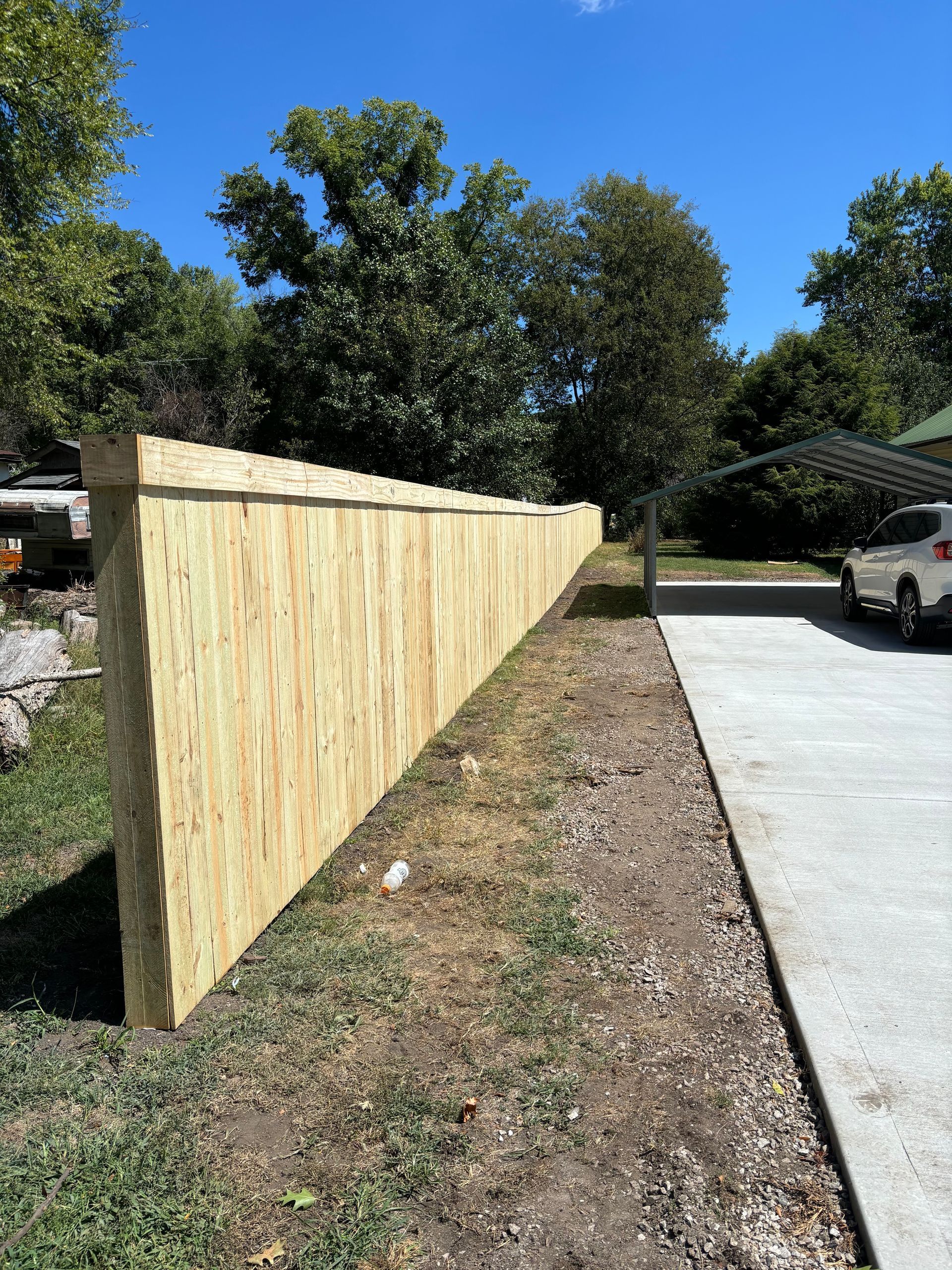 A wooden fence is sitting next to a concrete driveway.