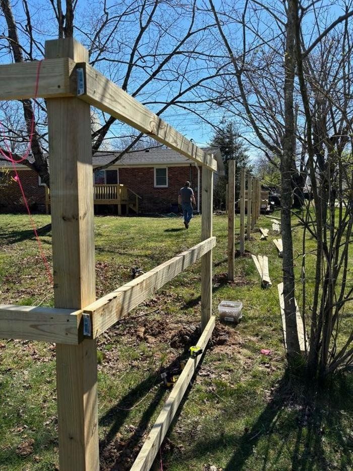A wooden fence is being built in a yard in front of a house.