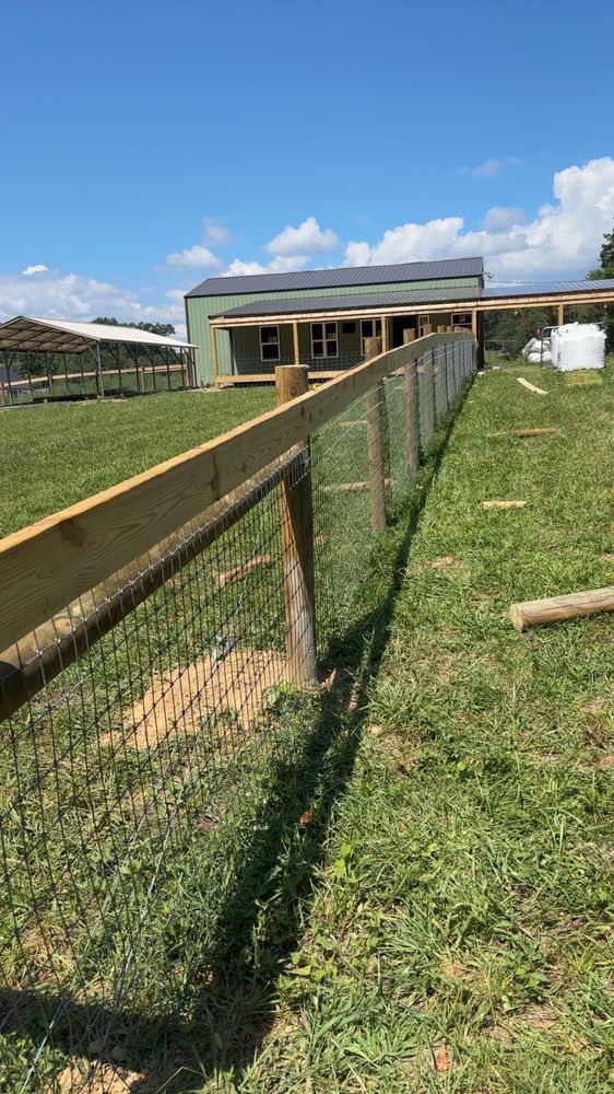 A wooden fence surrounds a grassy field with a house in the background.