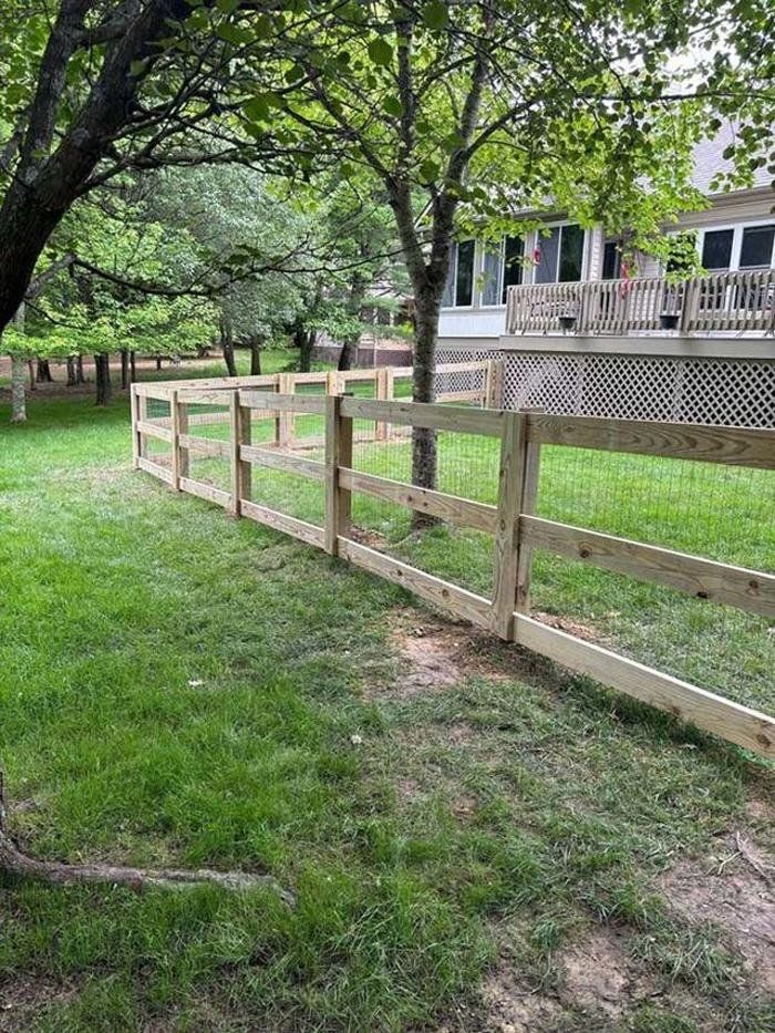 A wooden fence surrounds a lush green yard in front of a house.