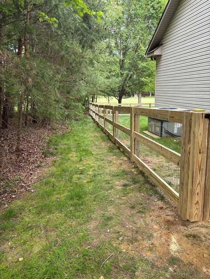 A wooden fence along a grassy path next to a house.